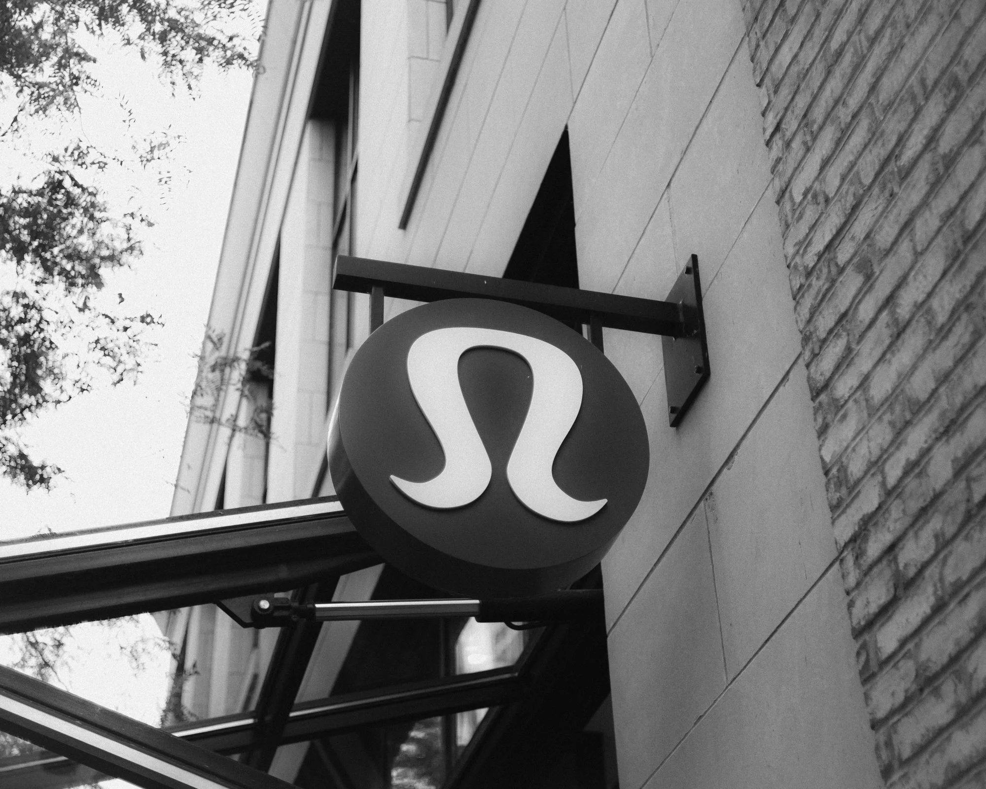 A wine bar or restaurant sign featuring a circular logo with a stylized letter 'L' in white, mounted on a metal bracket on a building with brick and painted exterior walls.