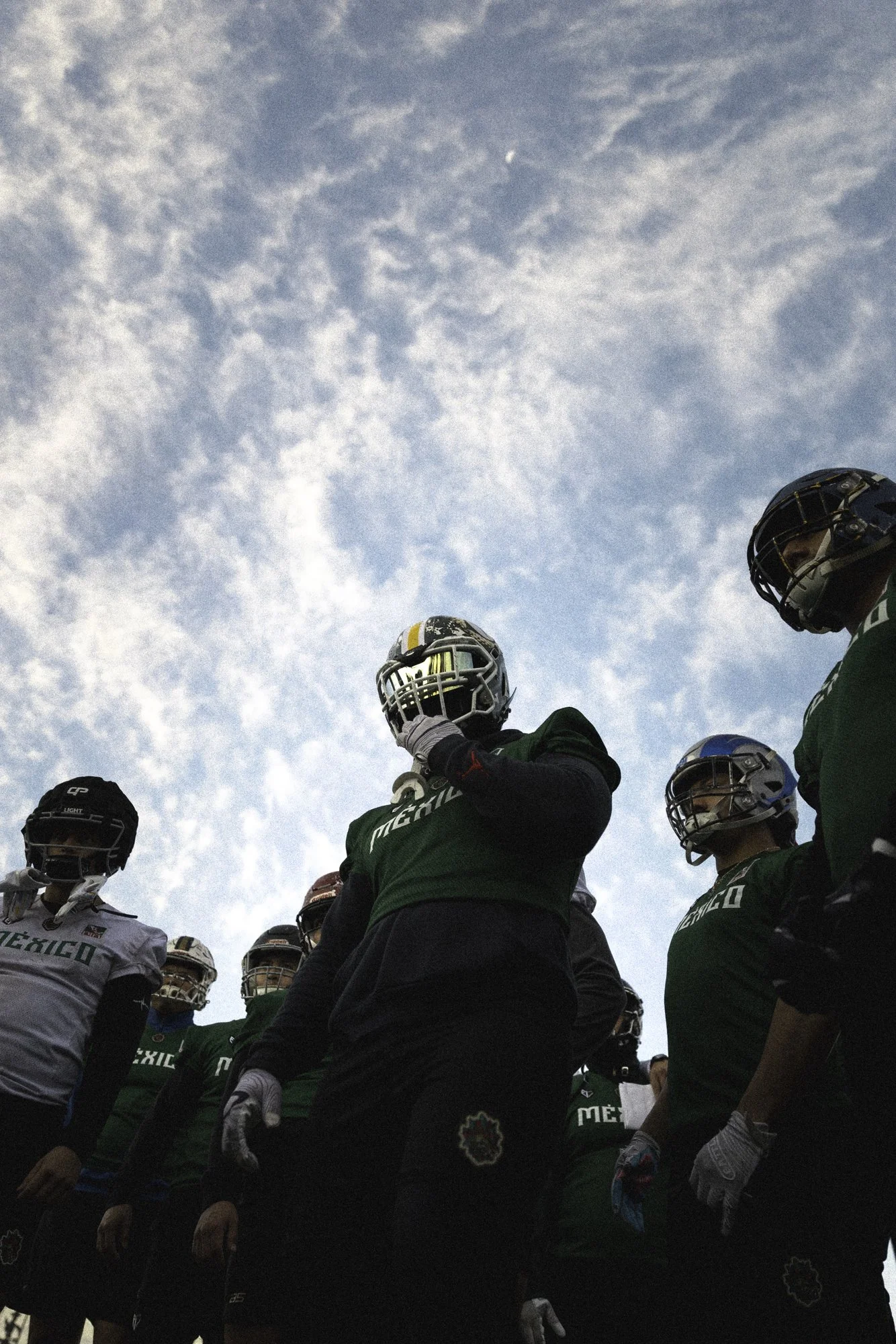 A group of football players wearing helmets and uniforms standing outdoors against a sky with clouds.