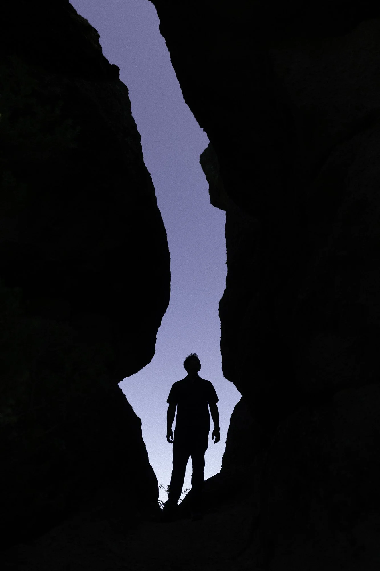Person standing between tall, dark rock formations with a clear sky visible above.