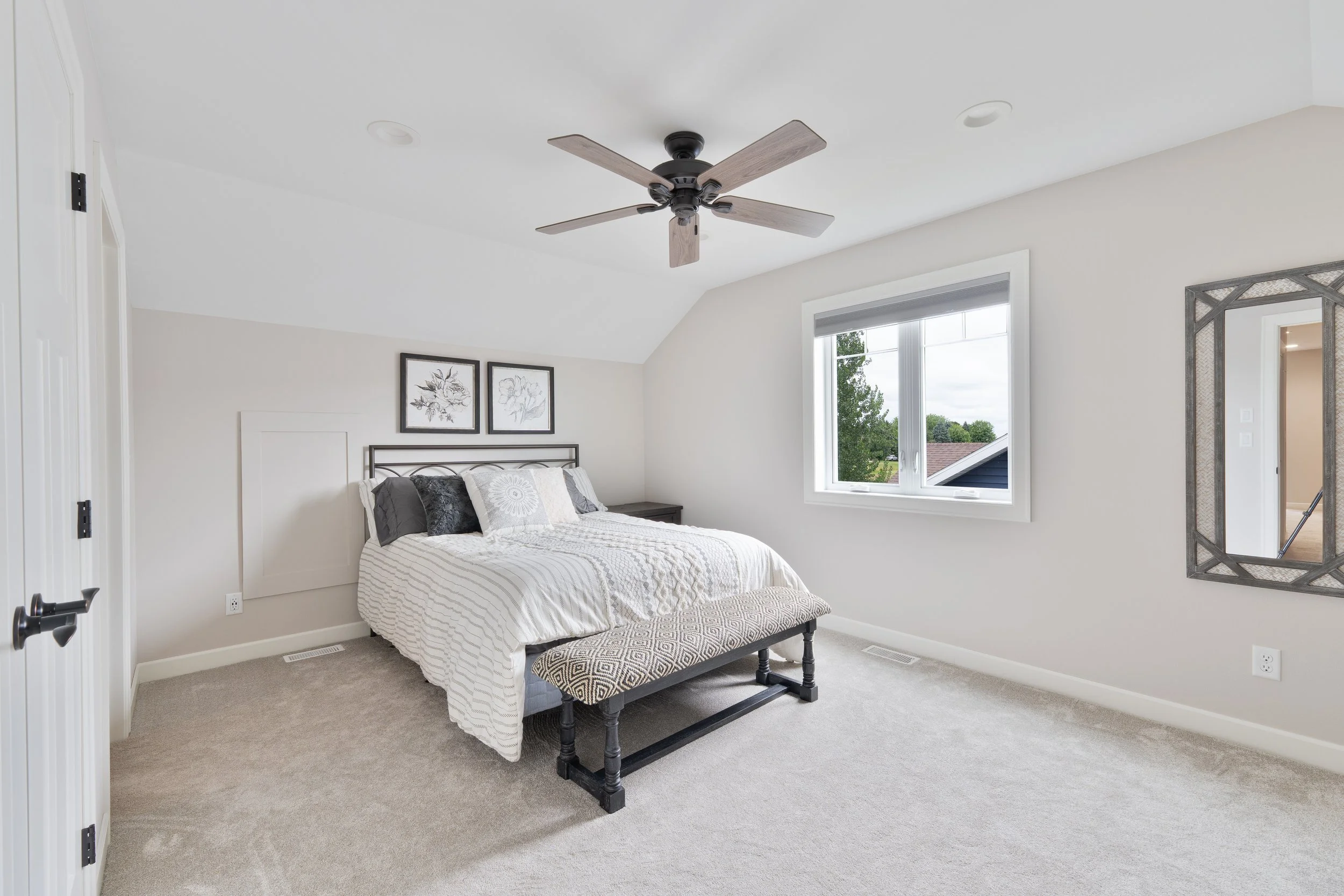 Bedroom with a bed, window, ceiling fan, mirror, and neutral decor.