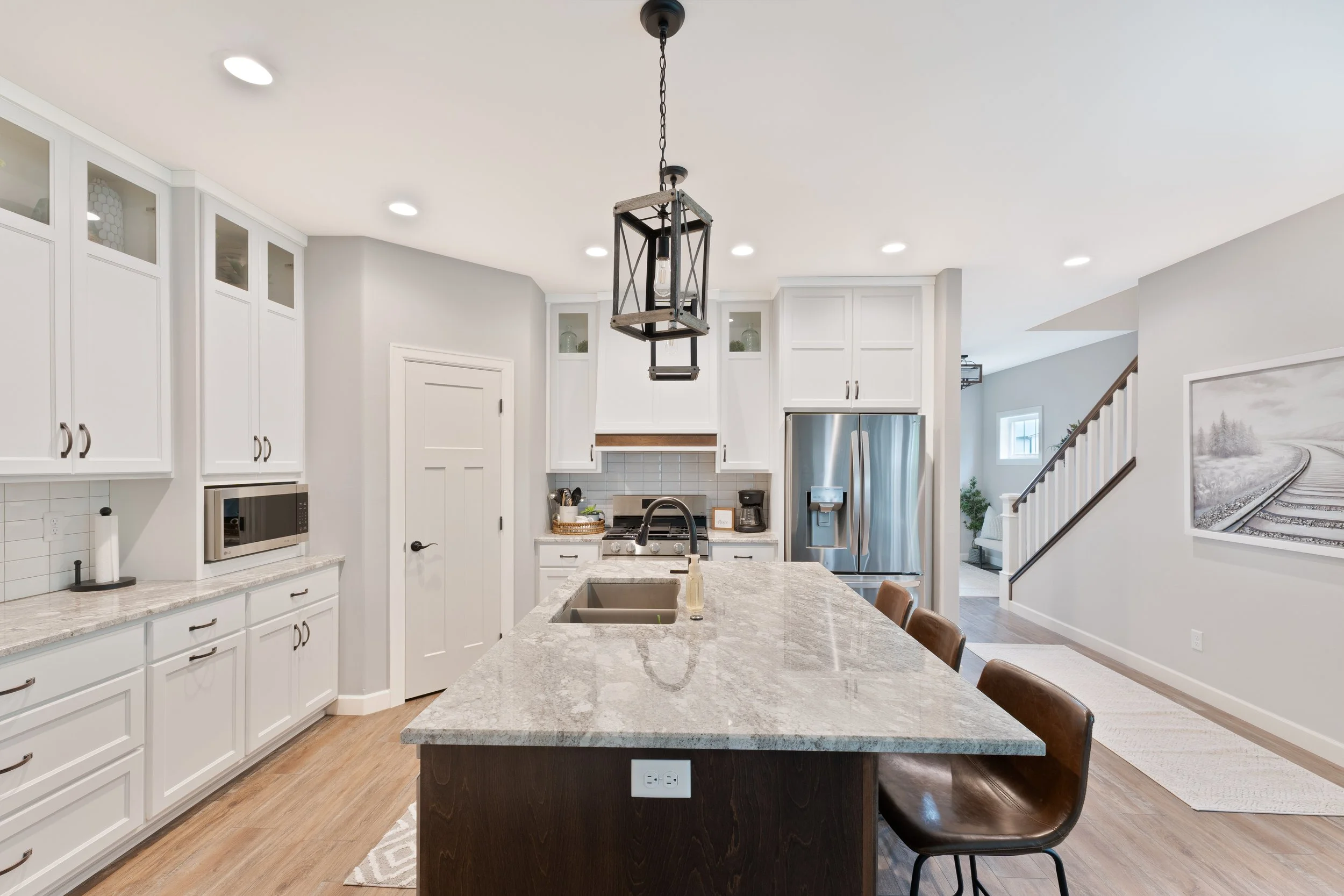 Modern kitchen with white cabinets, granite island, stainless steel refrigerator, and a pendant light fixture