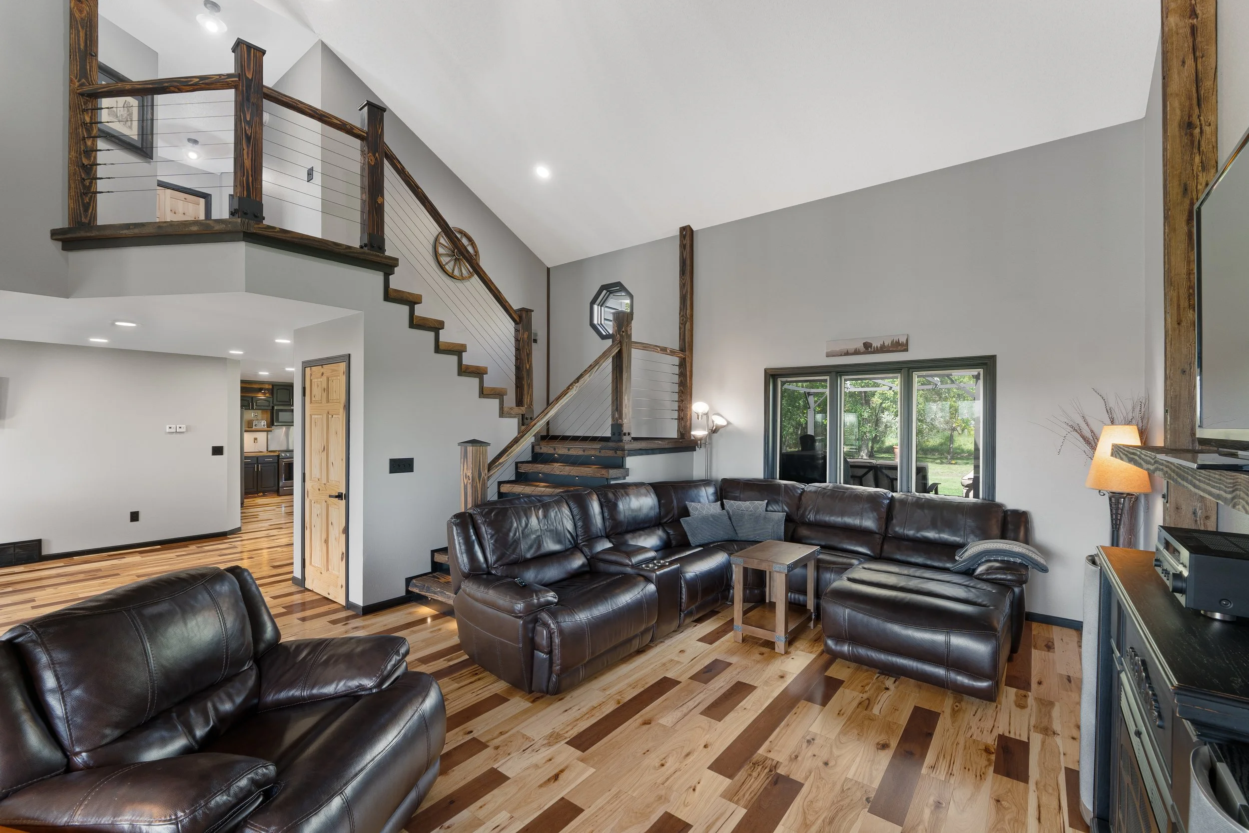 Living room with leather sectional sofas, wooden accents, and large windows, showcasing a cozy and rustic interior style.