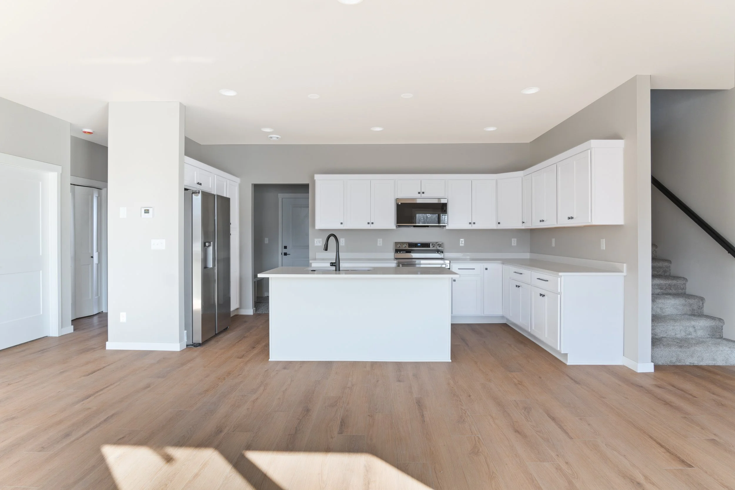 Modern kitchen with white cabinets, stainless steel appliances, a central island with a sink, and light wood flooring.