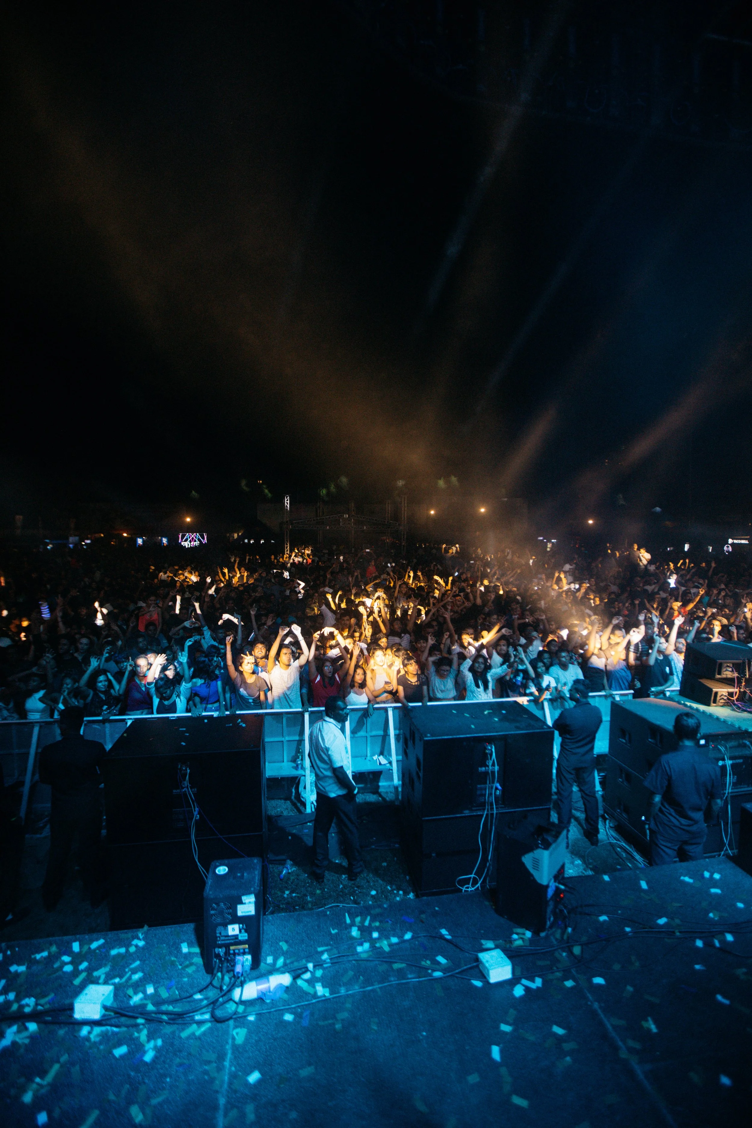 Crowd dancing at a concert or festival at night with stage lights in the background.