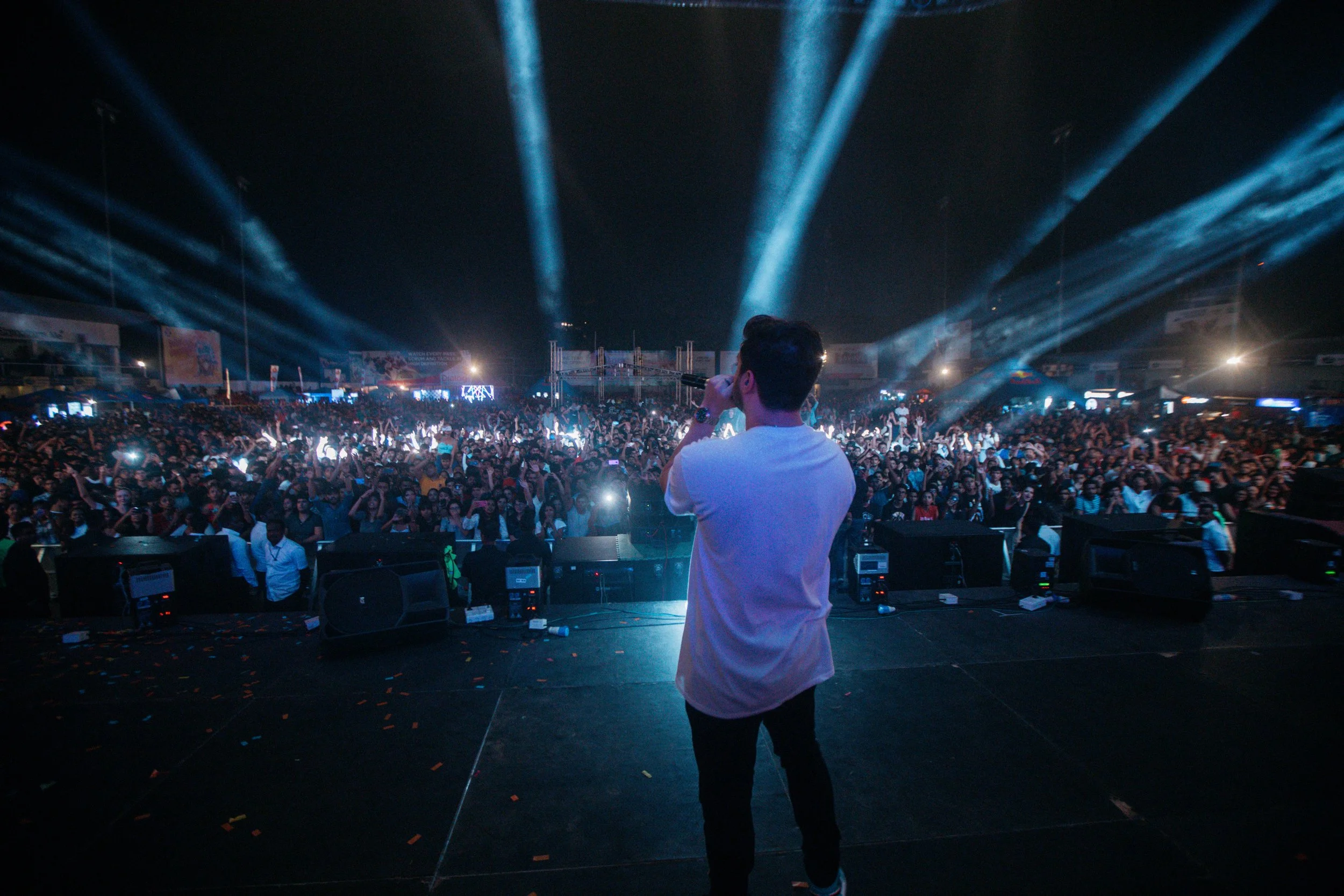 Performer on stage at a concert with large crowd, bright stage lights, and fog.