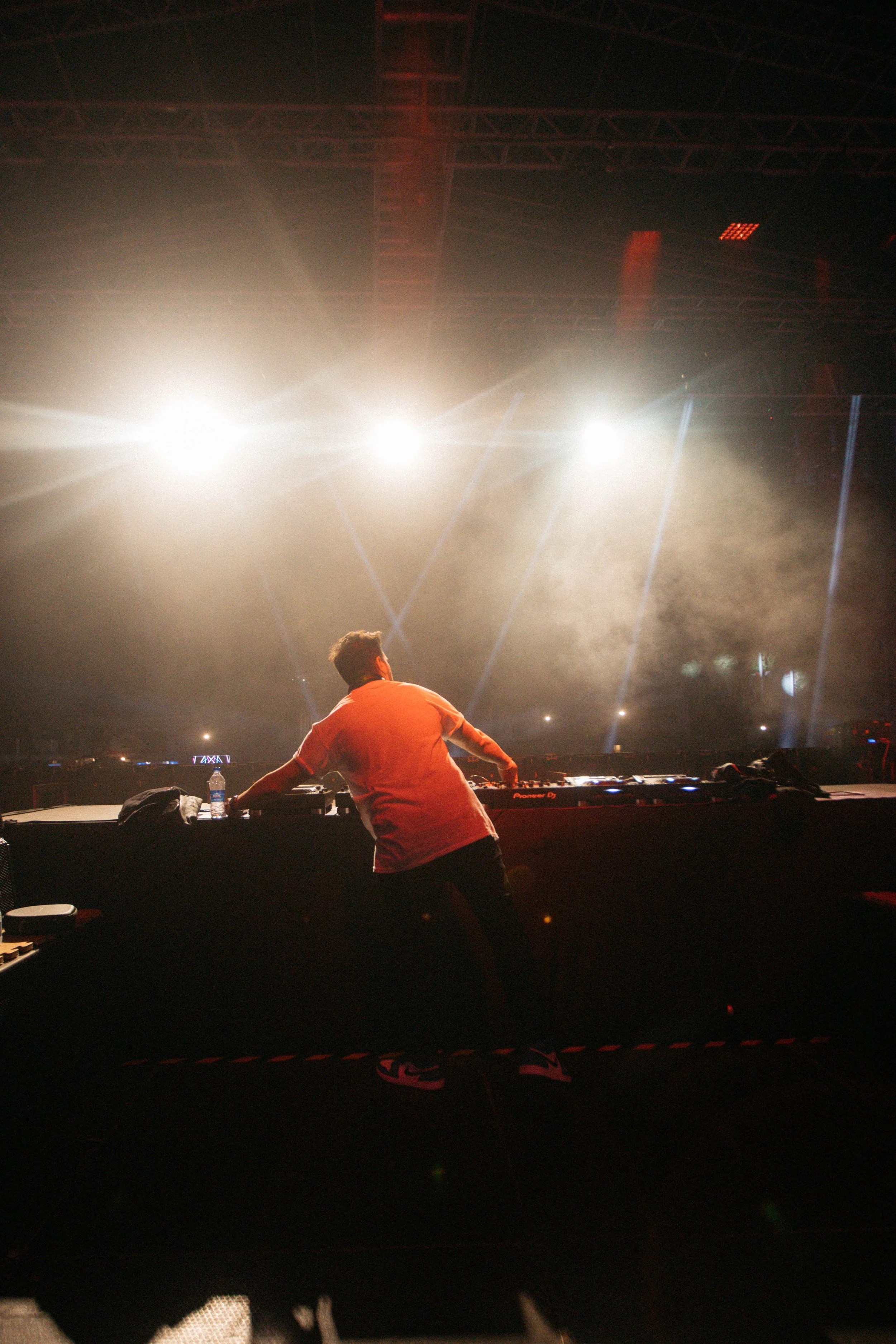 A DJ performing at a concert with bright stage lights and laser effects in the background.