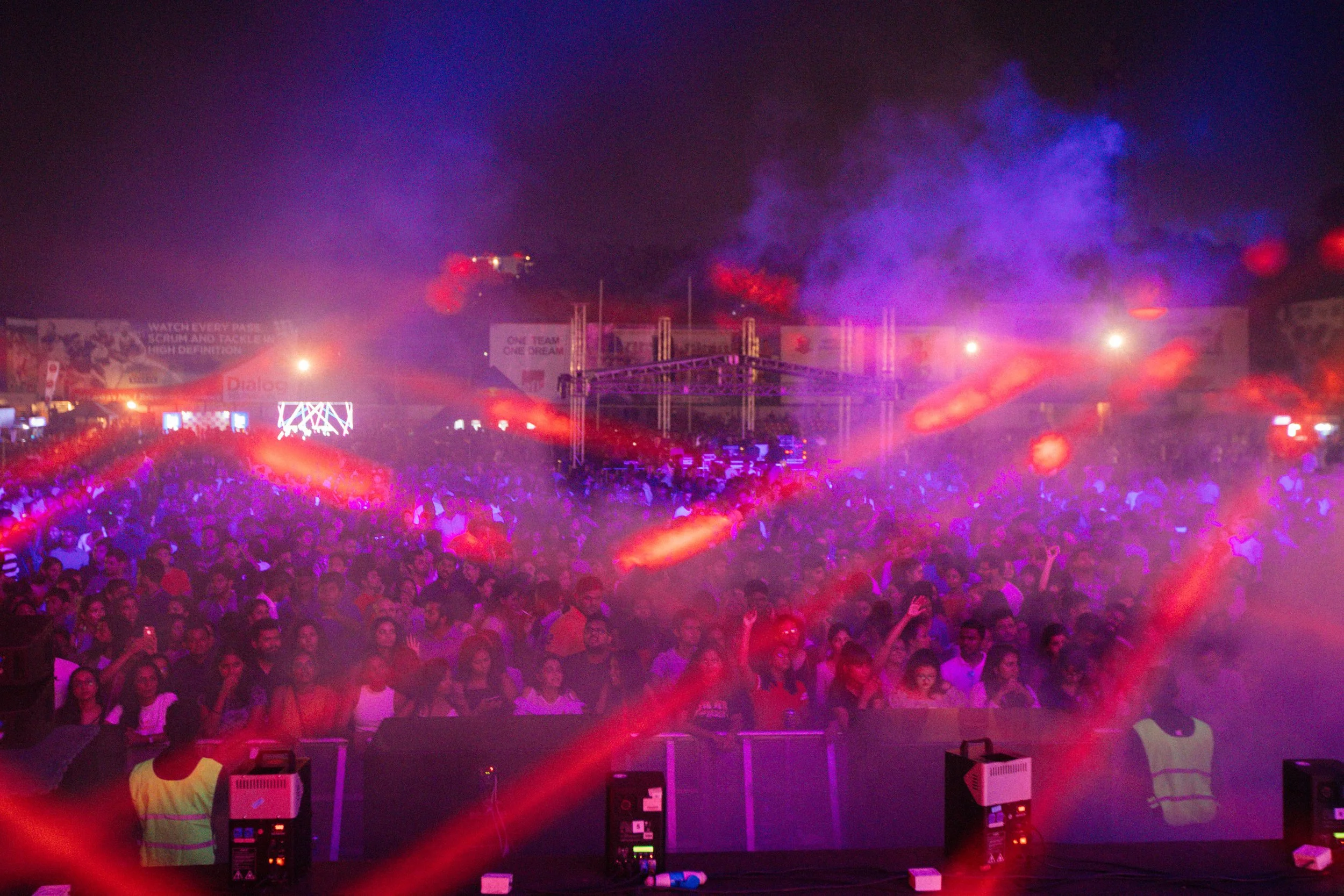 Crowd at a concert or festival with colorful stage lights and smoke effects.