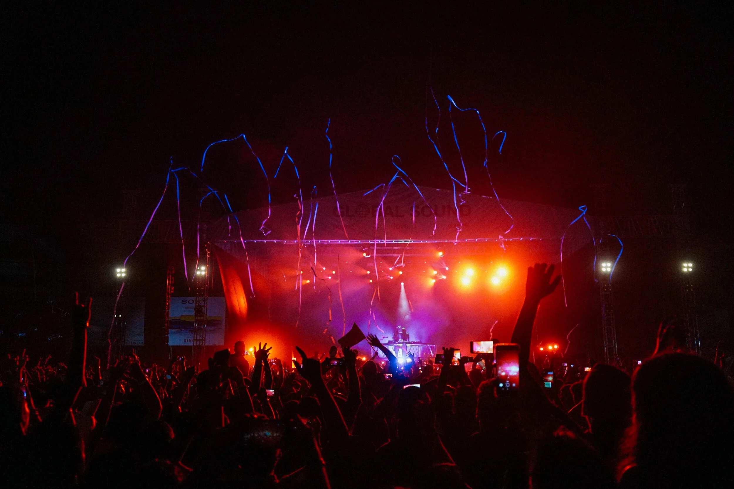 Crowd attending a concert or music festival at night with stage lights, balloons, and streamers in the air.