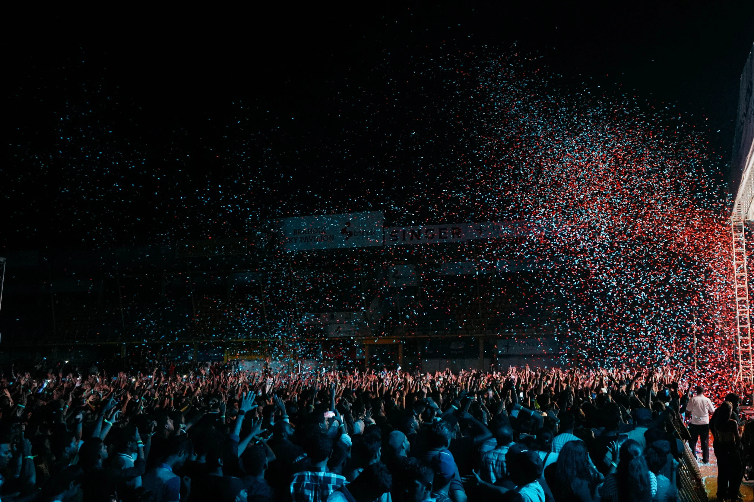 Crowd of people at a concert with red and blue confetti in the air at night.