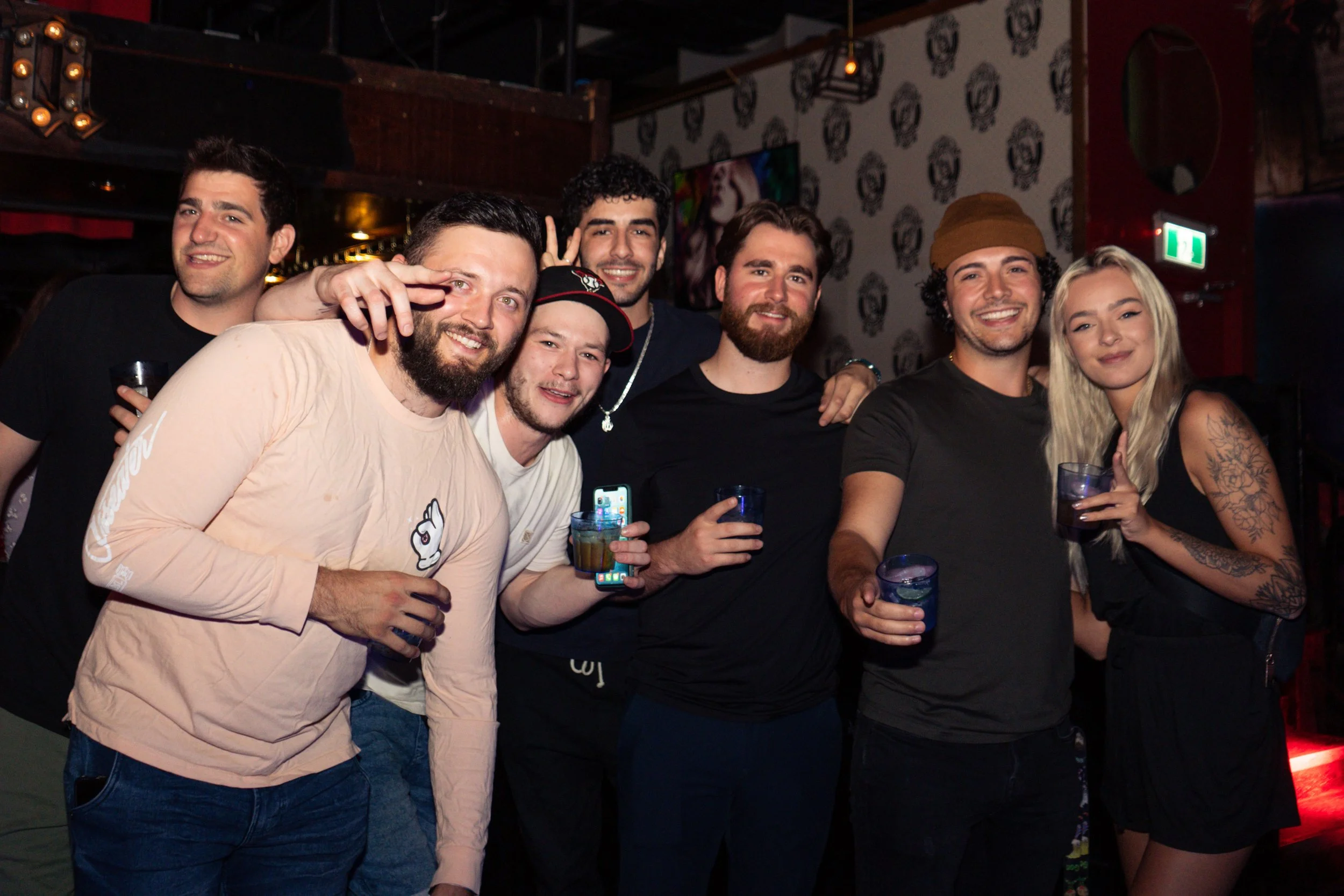 Group of young friends enjoying drinks at a bar or nightclub, smiling and posing for a photo.