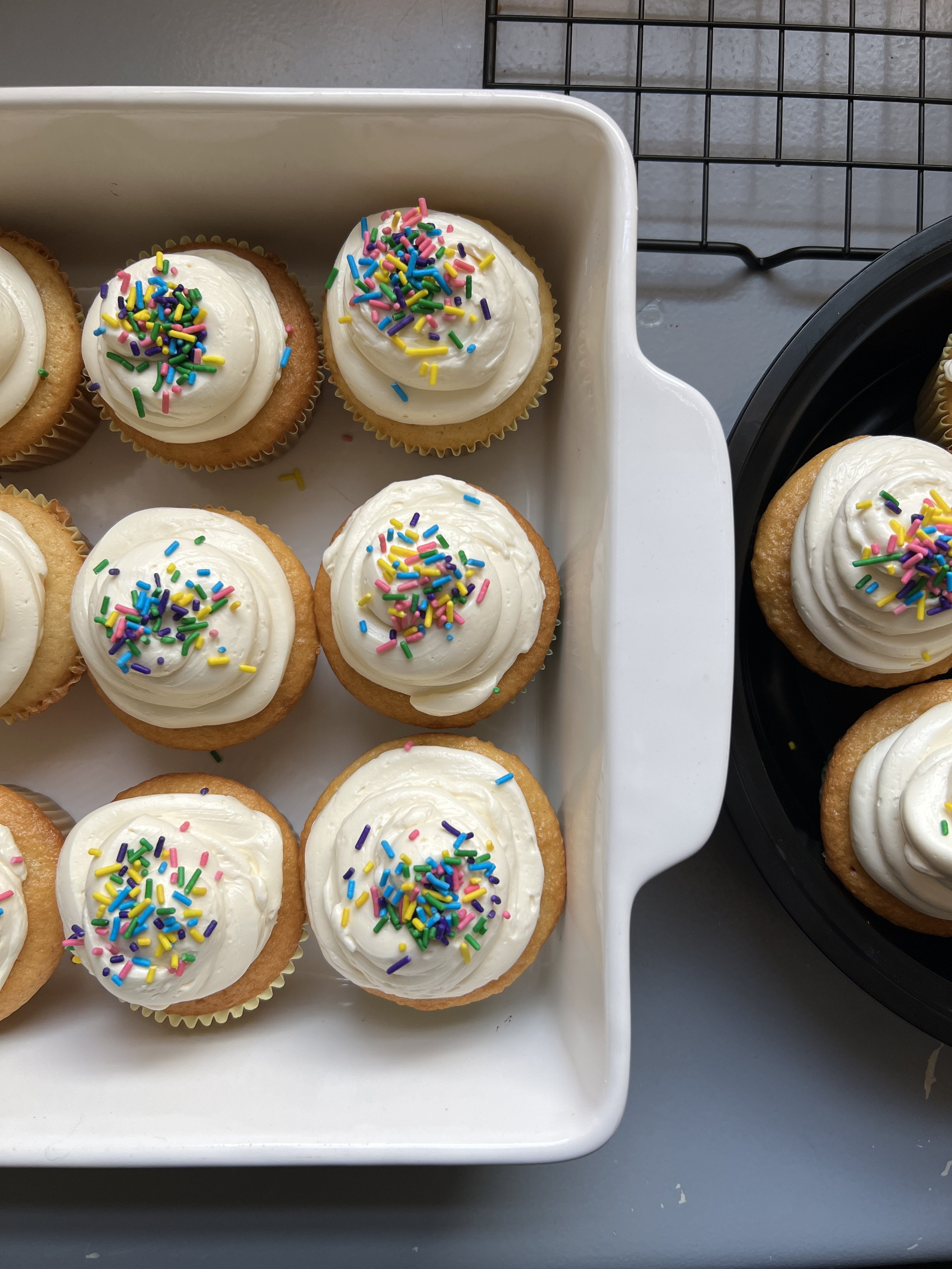 Cupcakes with white frosting and colorful sprinkles on top, arranged on a white tray.