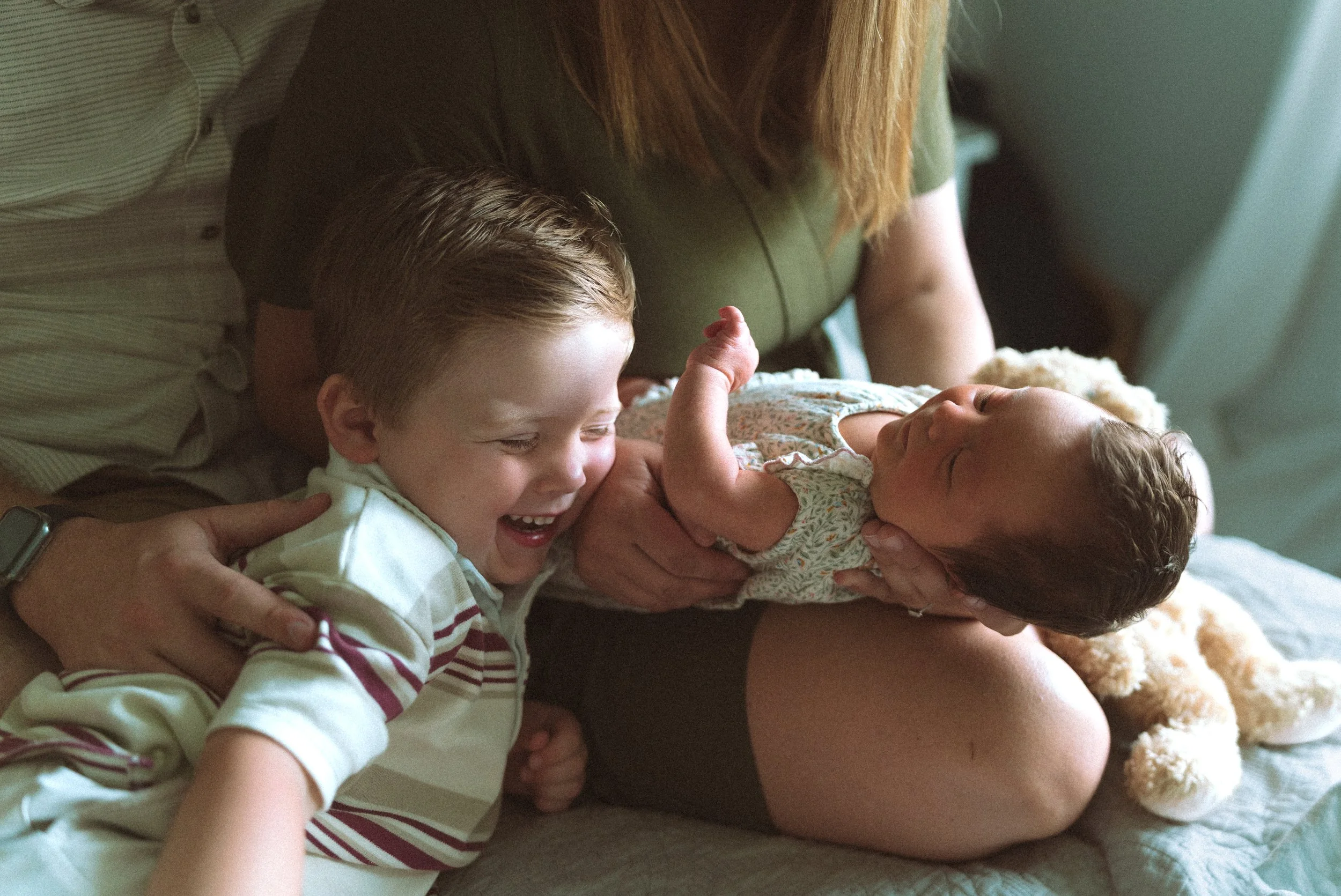 A woman holding a smiling young boy and a baby girl, all lying on a bed together.