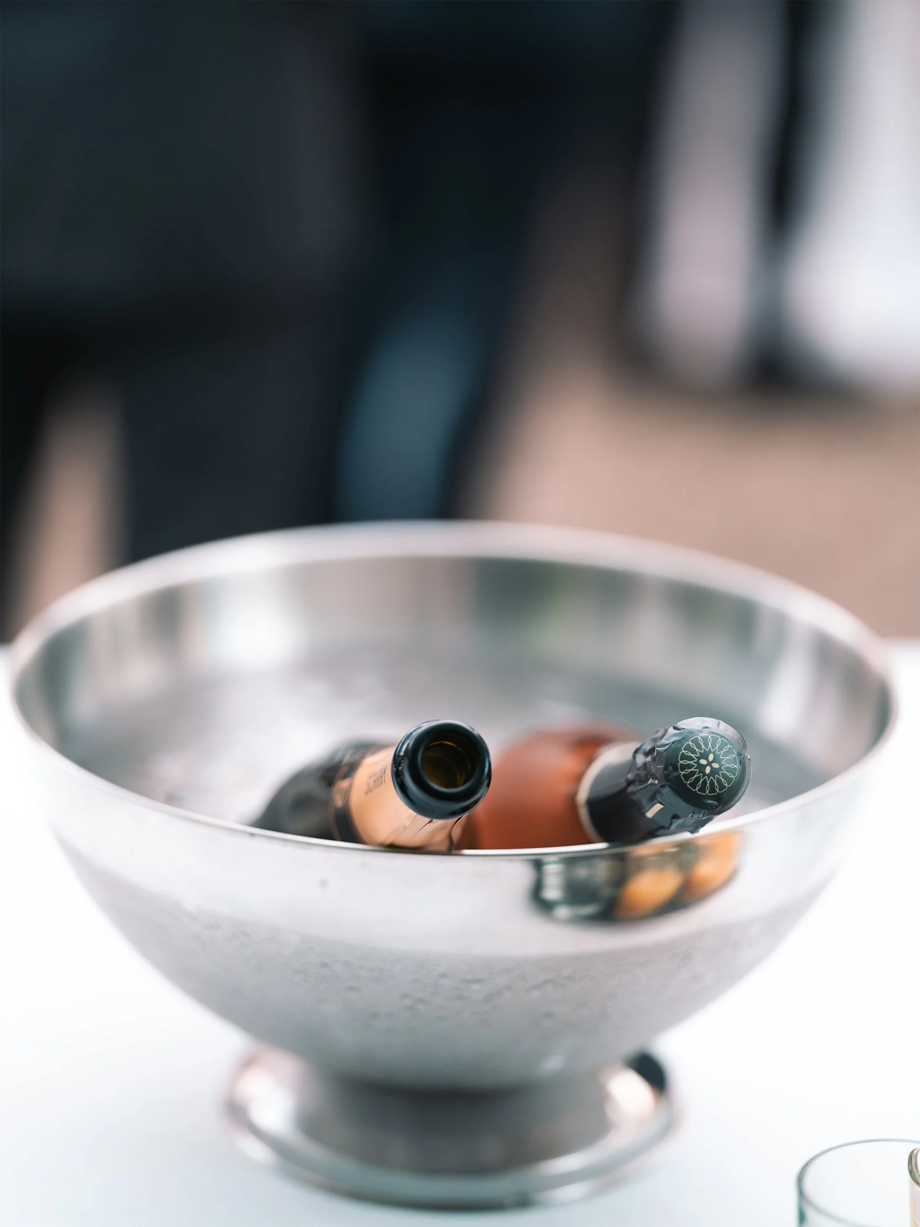 Zwei Crémant-Flaschen kühlen in einem silbernen Sektkühler auf einer weißen Tafel.