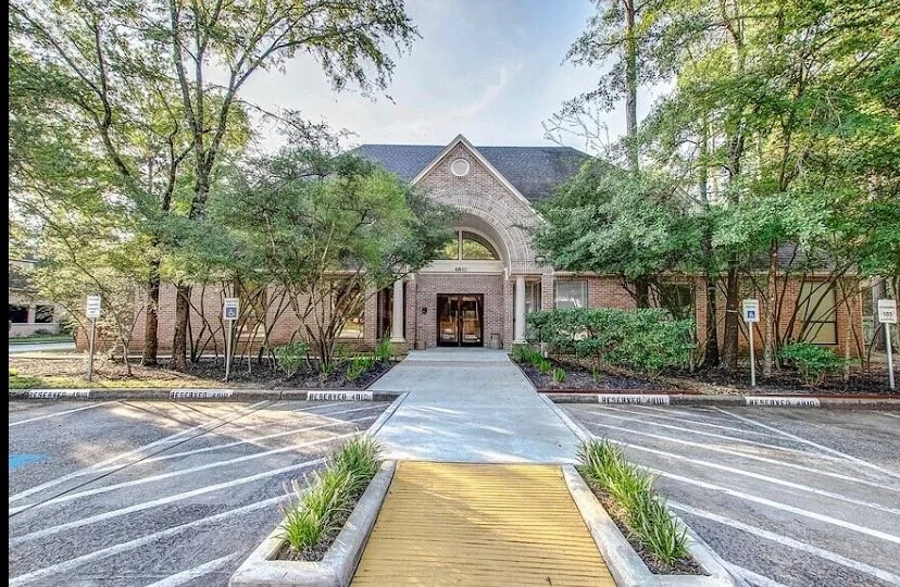 Residential building with stone and brick facade, surrounded by trees, with a concrete walkway leading to the entrance, and parking spaces on either side labeled 'Reserved.'