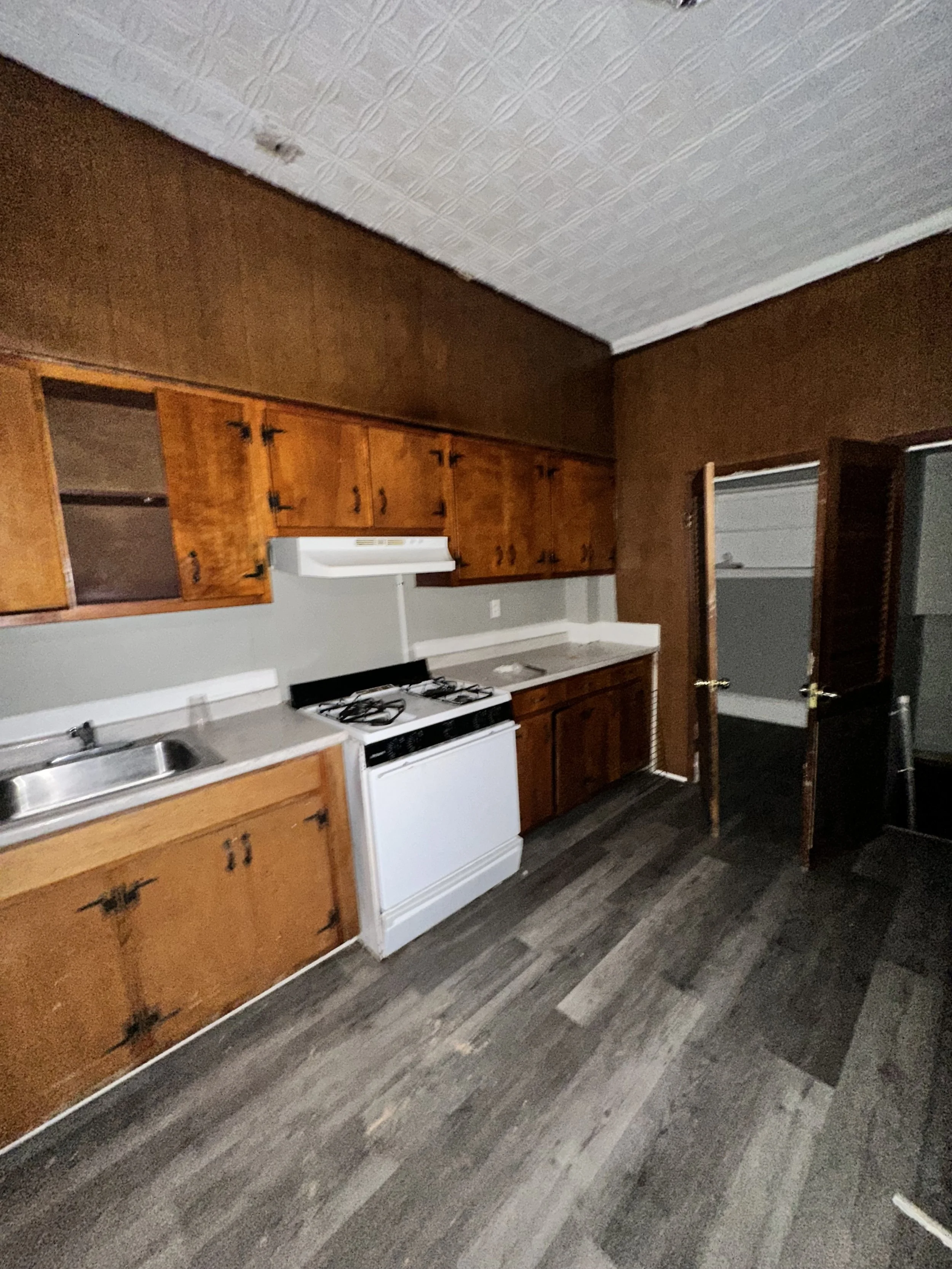 Kitchen with wooden cabinets, a white stove, a sink, and a partially open door leading to an adjacent room.
