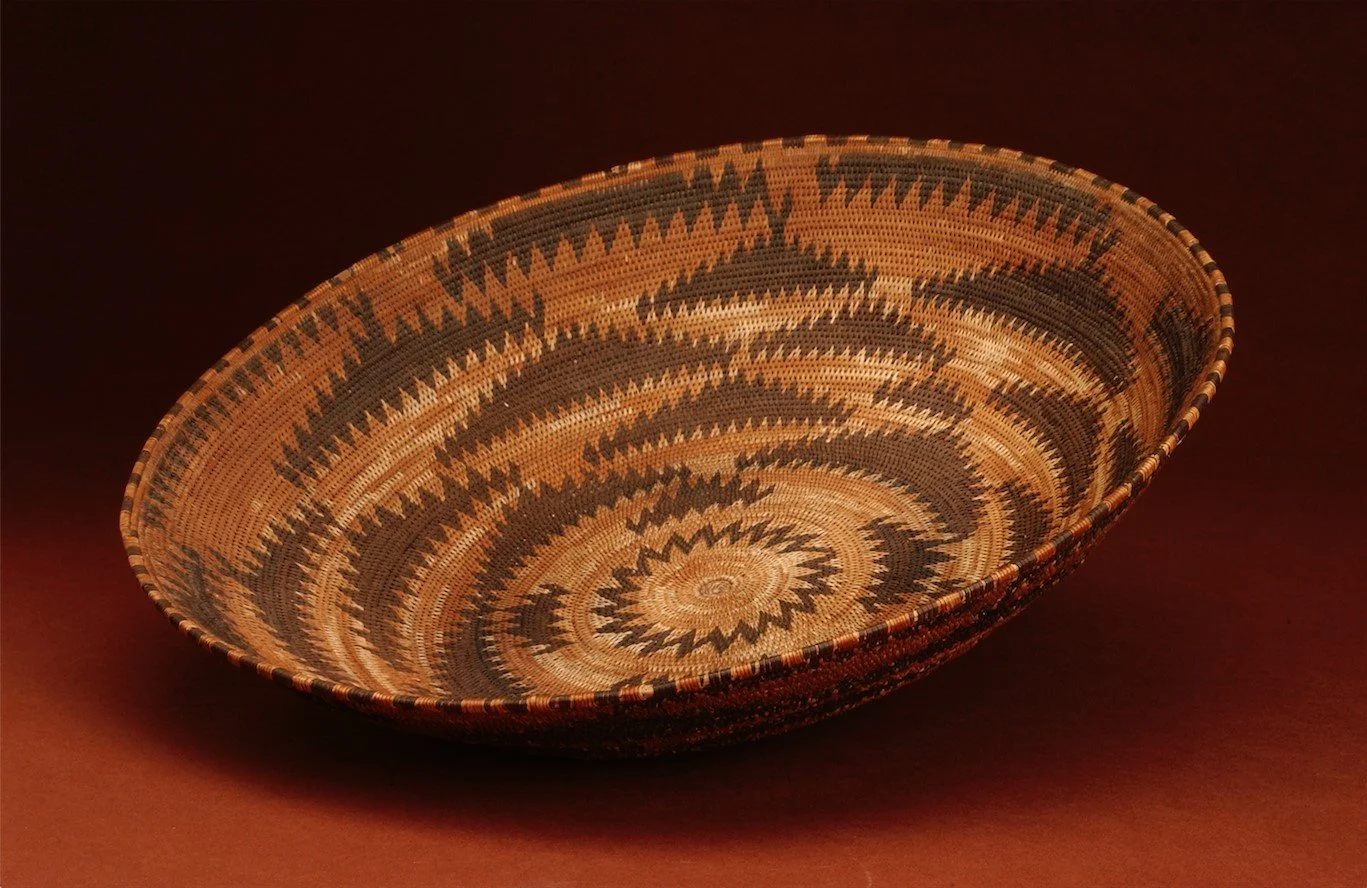 Pomo basket with an elaborate woven pattern made from red, dark, and light tan reeds.
