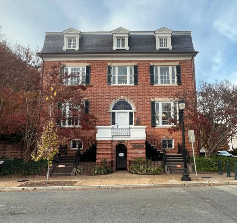 Color photograph of Belmont-Paul Women's Equality National Monument. It is a symmetrical red brick building with three dormer windows and rows of rectangular windows across the facade.