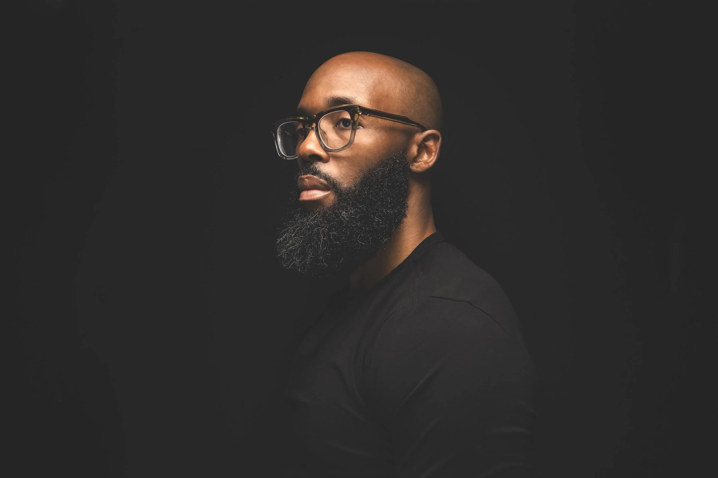 Portrait of a man with glasses and a full beard, looking to the side against a dark background.