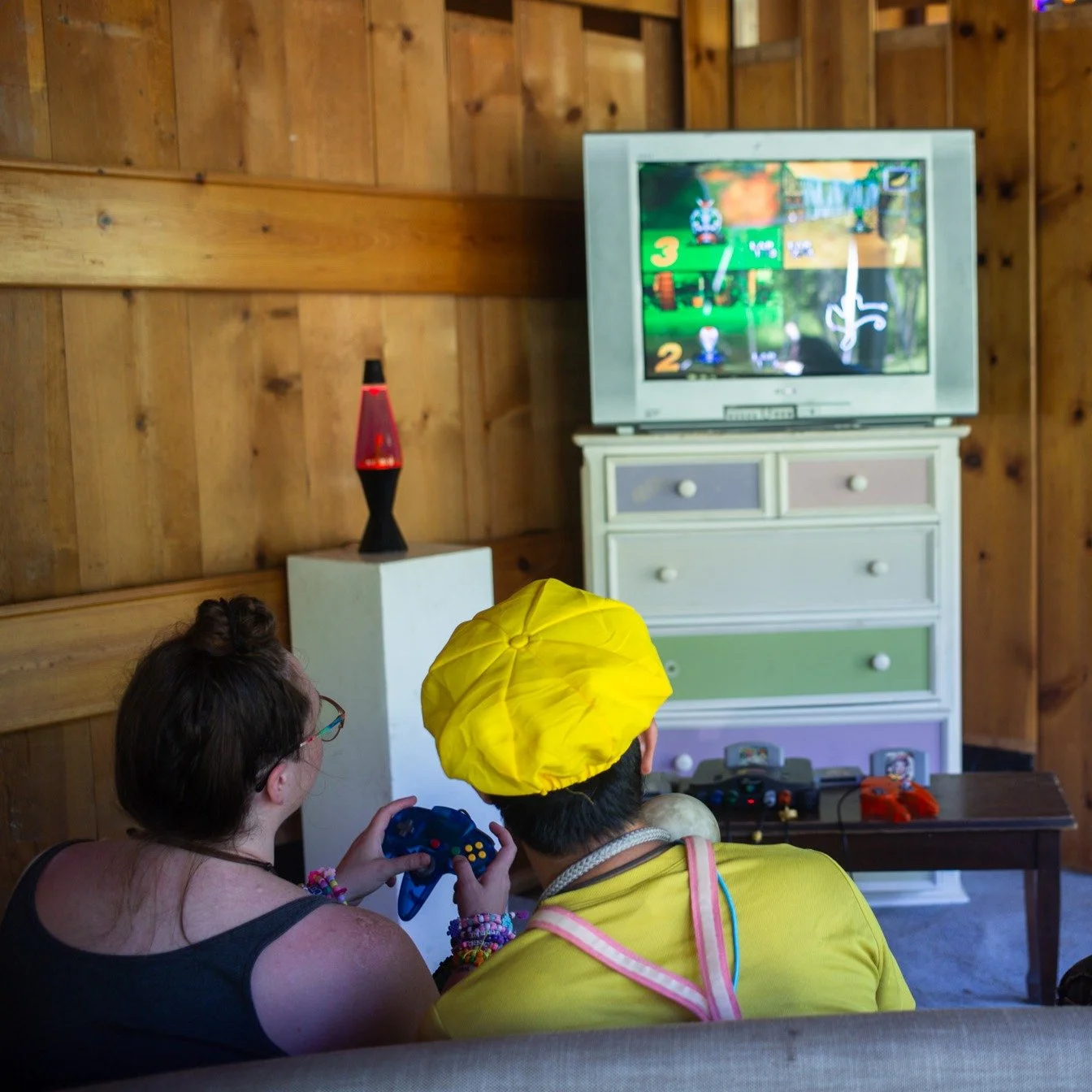 Two people sitting on a couch playing a video game together, with a TV screen in front of them showing a colorful game scene.