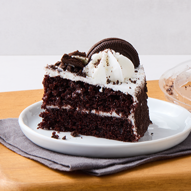 Chocolate cake with white frosting, whipped cream, and an Oreo cookie on top, served on a white plate.