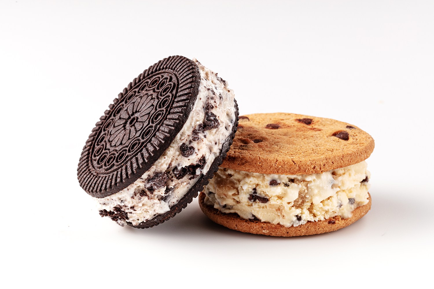Two ice cream sandwiches with cookies and chocolate ice cream, one with an Oreo cookie and the other with a chocolate chip cookie, on a white background.
