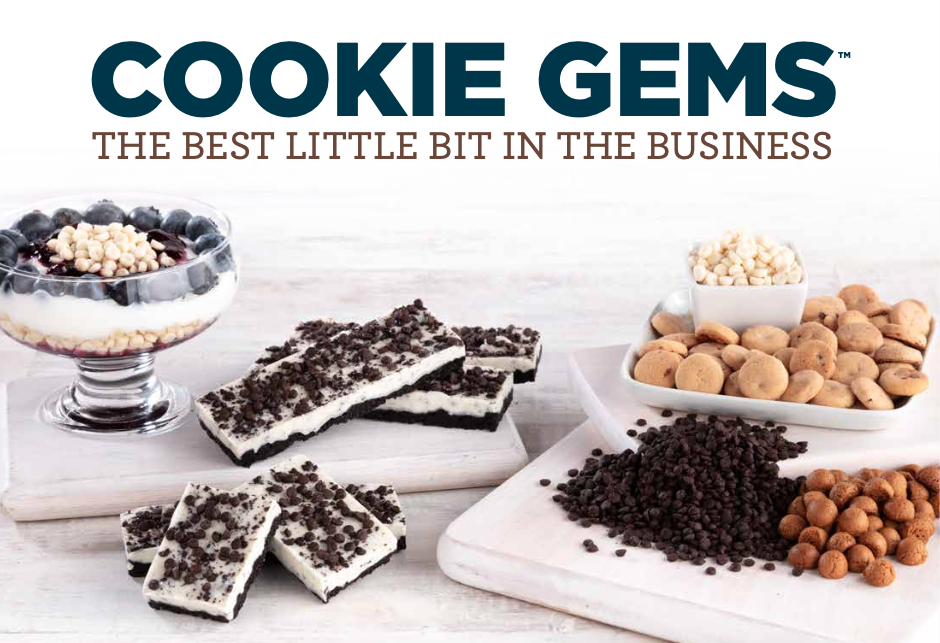 Display of various cookie ingredients and cookie bars, including white chocolate chip cookies, cookie bars with chocolate crumbs, and bowls of white chocolate chips, peanut butter chips, chocolate chips, and other cookie toppings on white wooden surfaces.