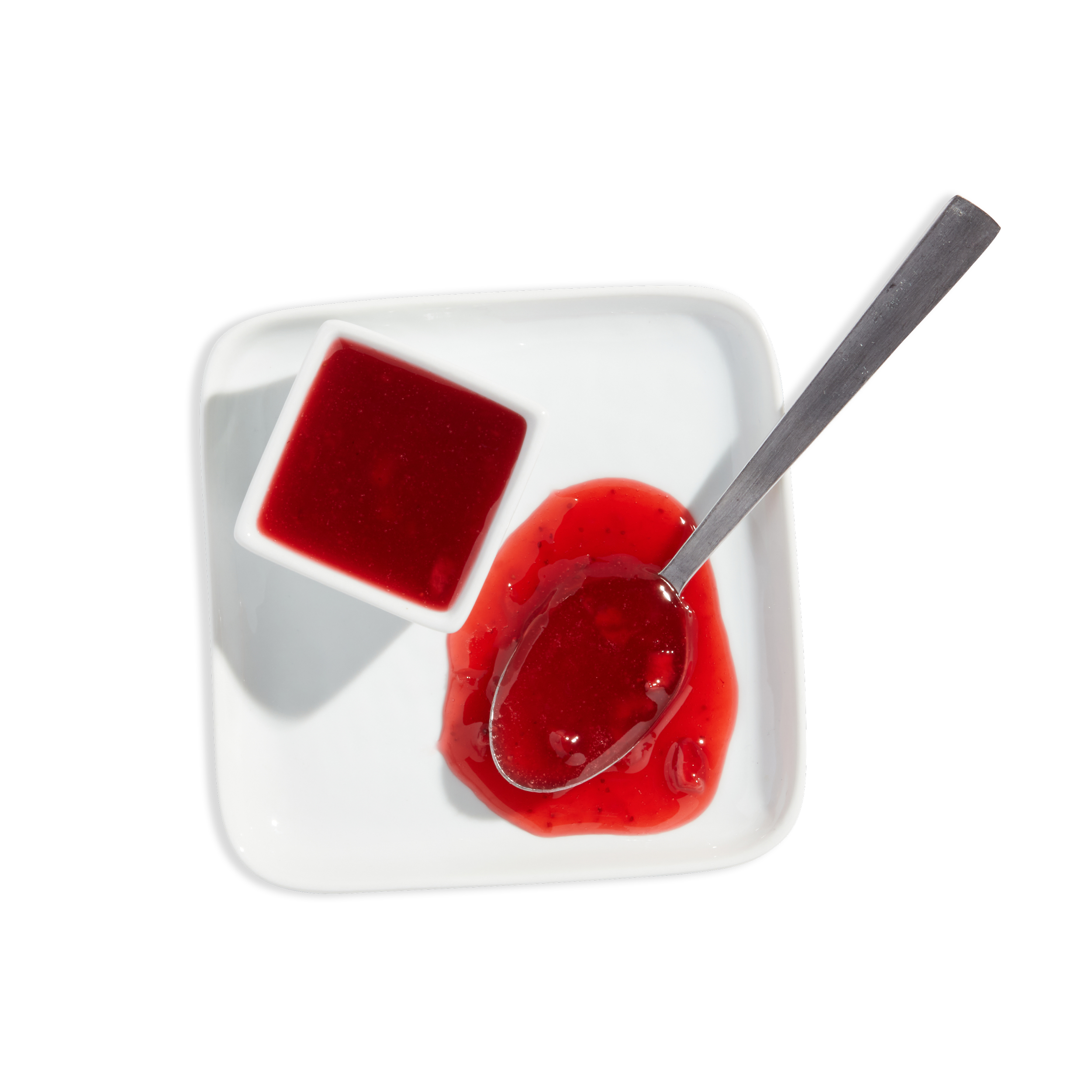 A white square plate with a small bowl of red fruit jelly, a spoon with red jelly on it, and spilled jelly on the plate.