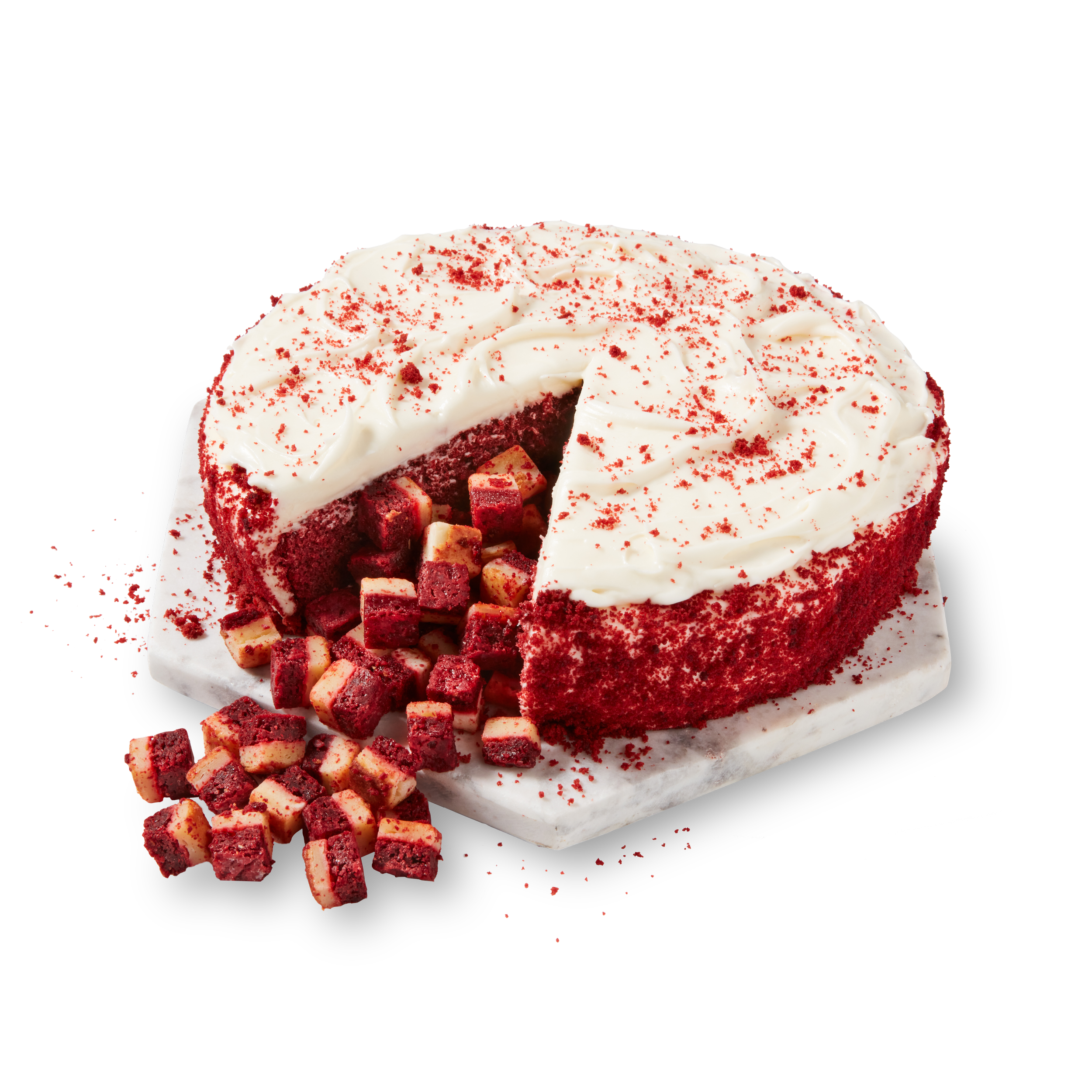 Red velvet cake with cream cheese frosting, sprinkled with red crumbs, with some cake cubes on a white marble surface.