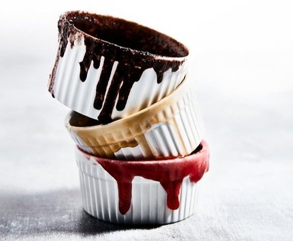 Three stacked cupcake liners with melted chocolate, caramel, and strawberry toppings