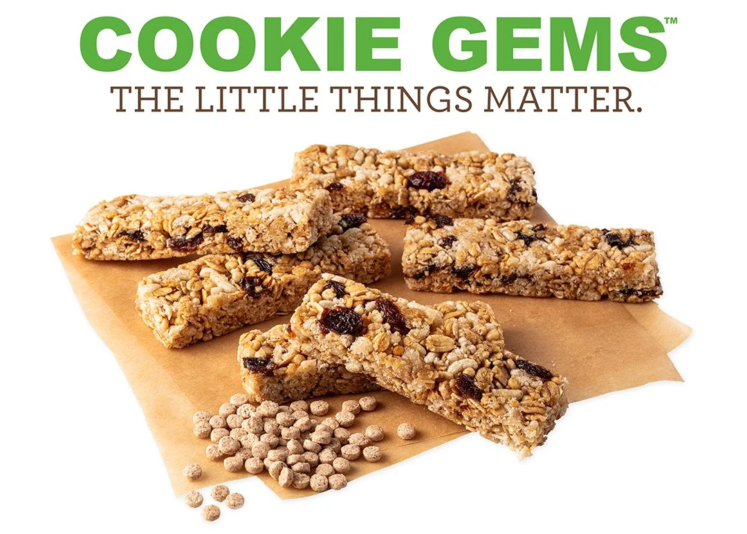 Close-up of granola bars with oats, dried berries, and nuts, placed on brown parchment paper, with loose cereal pieces nearby. Text stating "Cookie Gems" and "The Little Things Matter" is at the top of the image.