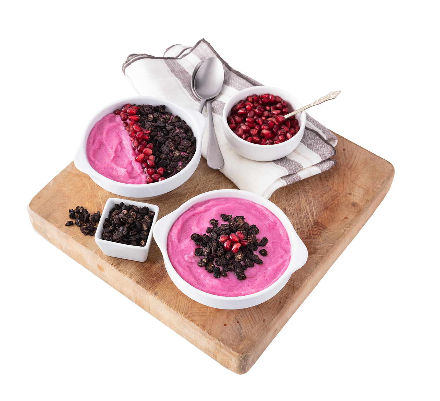 Two bowls of pink yogurt topped with pomegranate seeds and granola, one bowl of pomegranate seeds, and a small bowl of granola on a wooden cutting board with a spoon and striped napkin.