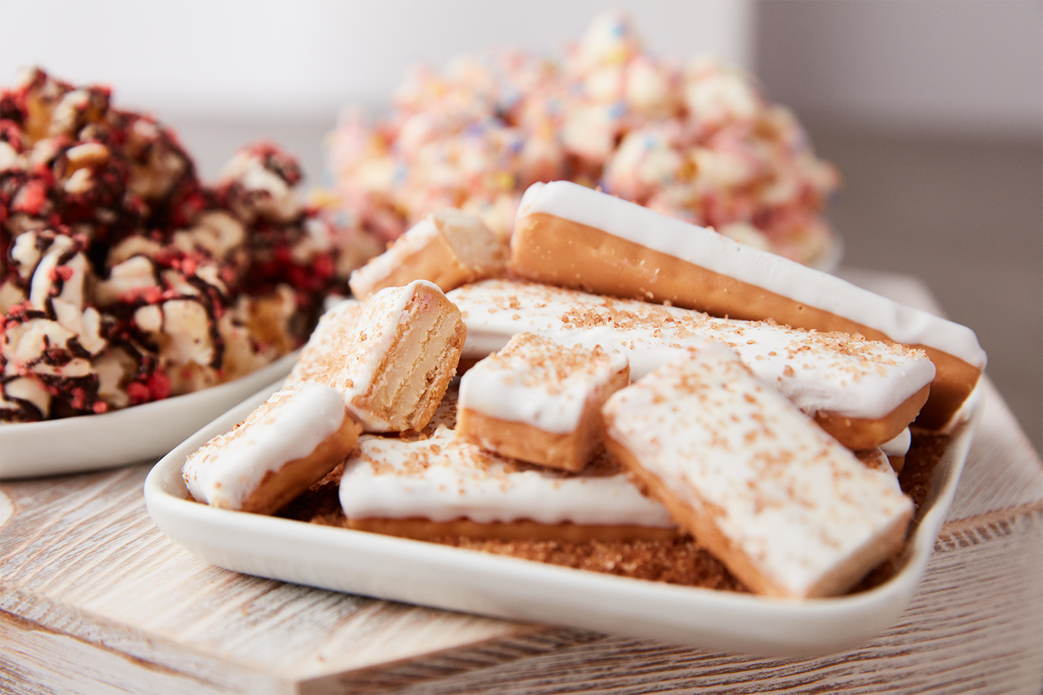 Plate of layered caramel and white icing cookies, with cookie chunks on top and sprinkled with crushed cookies, on a wooden surface.