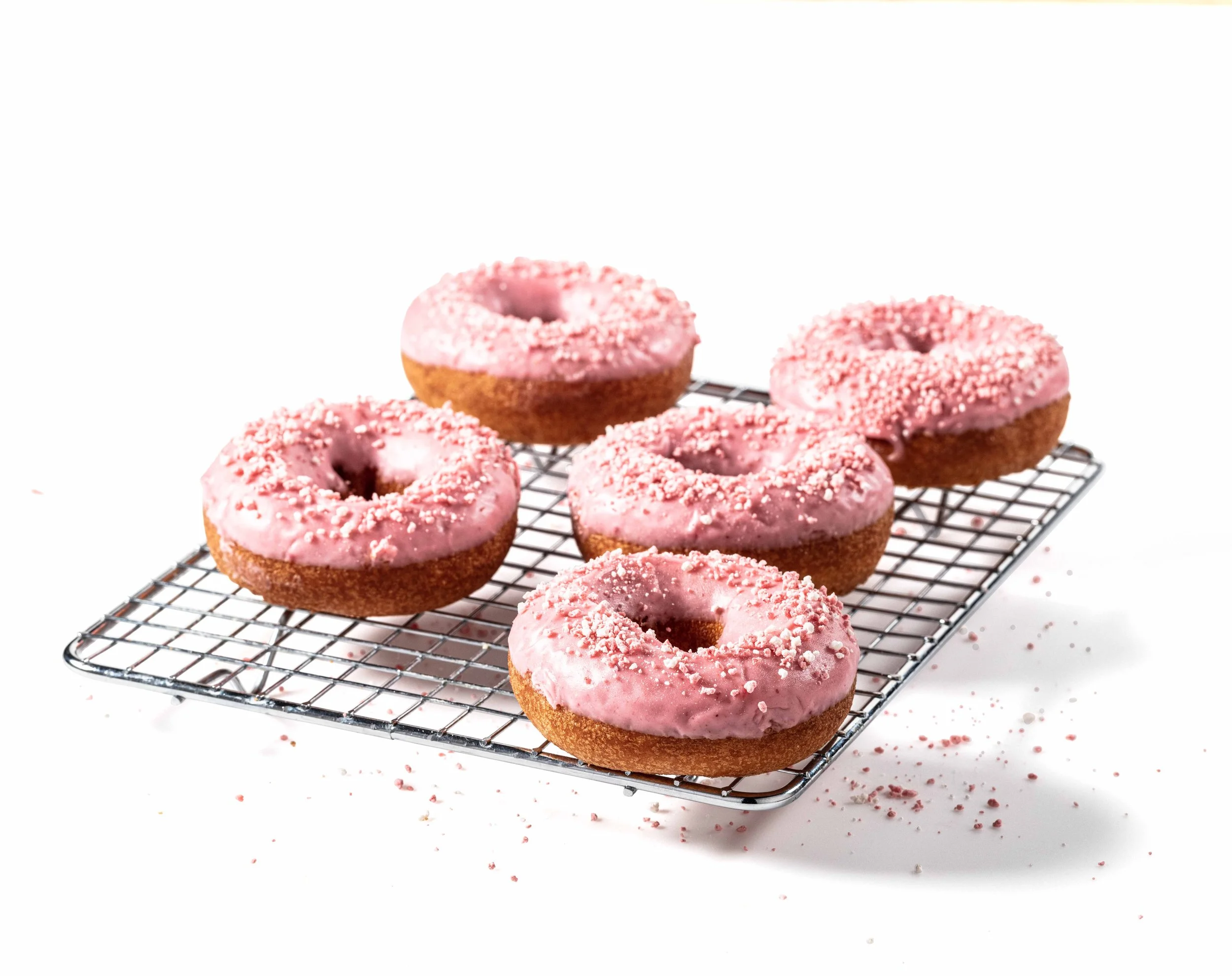 Six donuts with pink icing and sprinkles on a wire cooling rack.