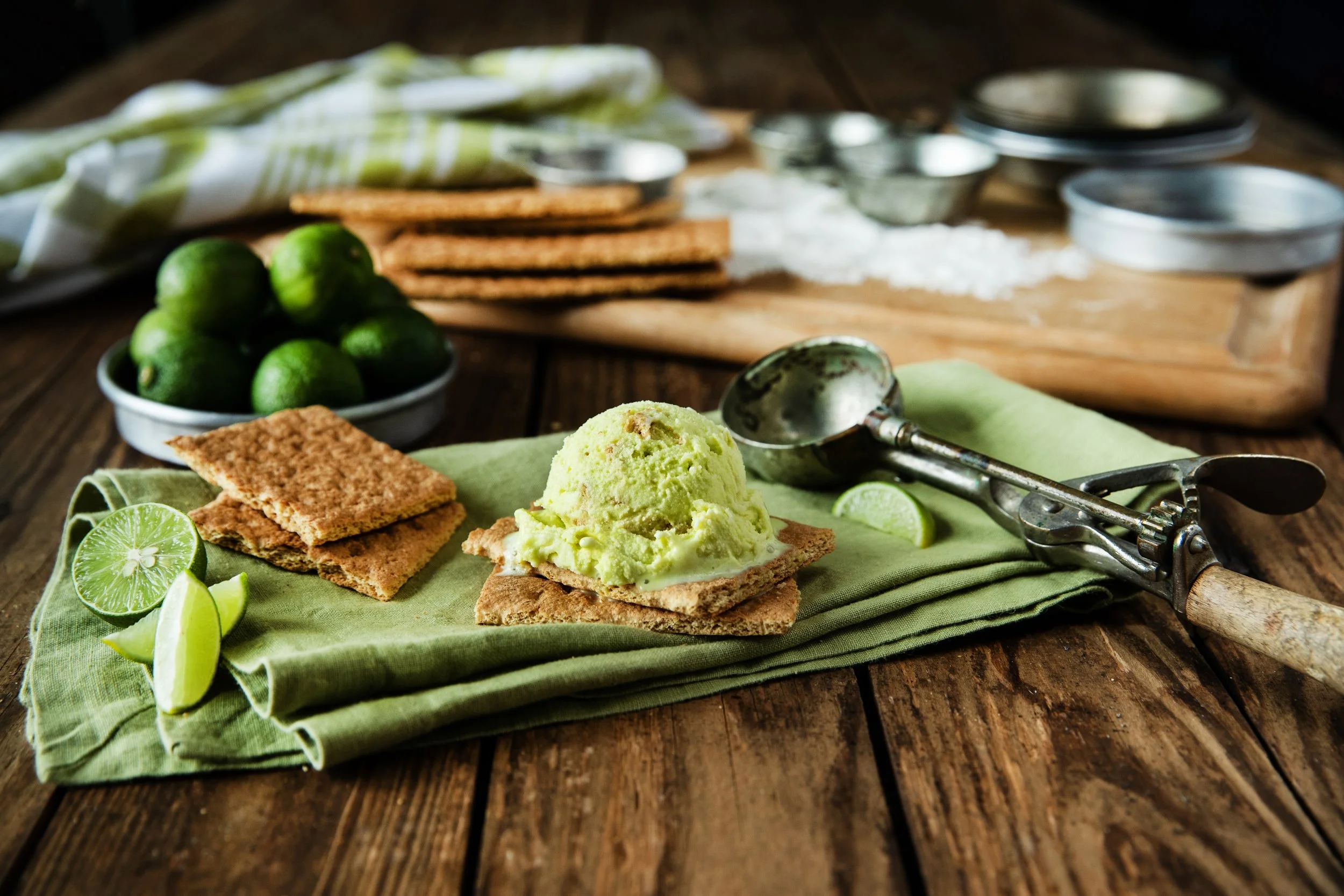 Lime-flavored sorbet on a cracker with lime wedges, crispy crackers, and lime in a rustic kitchen setting.