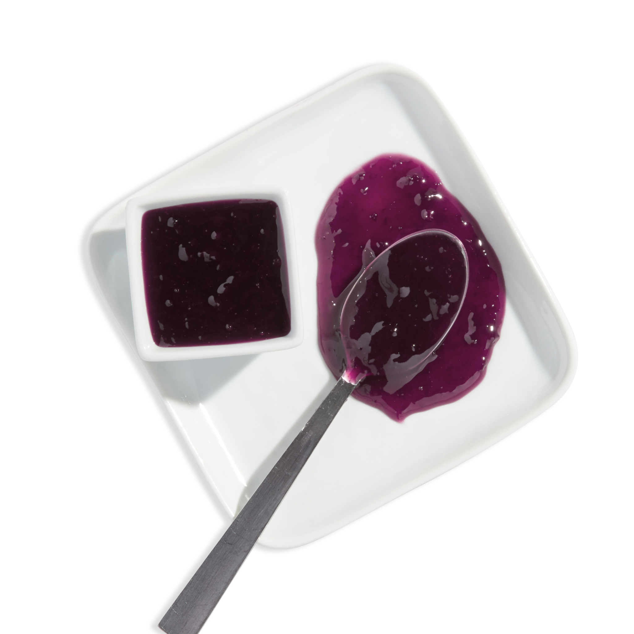 White plate with a small square dish of purple jelly and a spoon scooping purple jelly from a larger puddle of jelly.