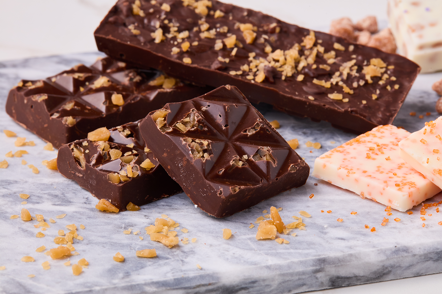 Assorted pieces of chocolate with nuts and white chocolate with orange sprinkles on a marble surface.