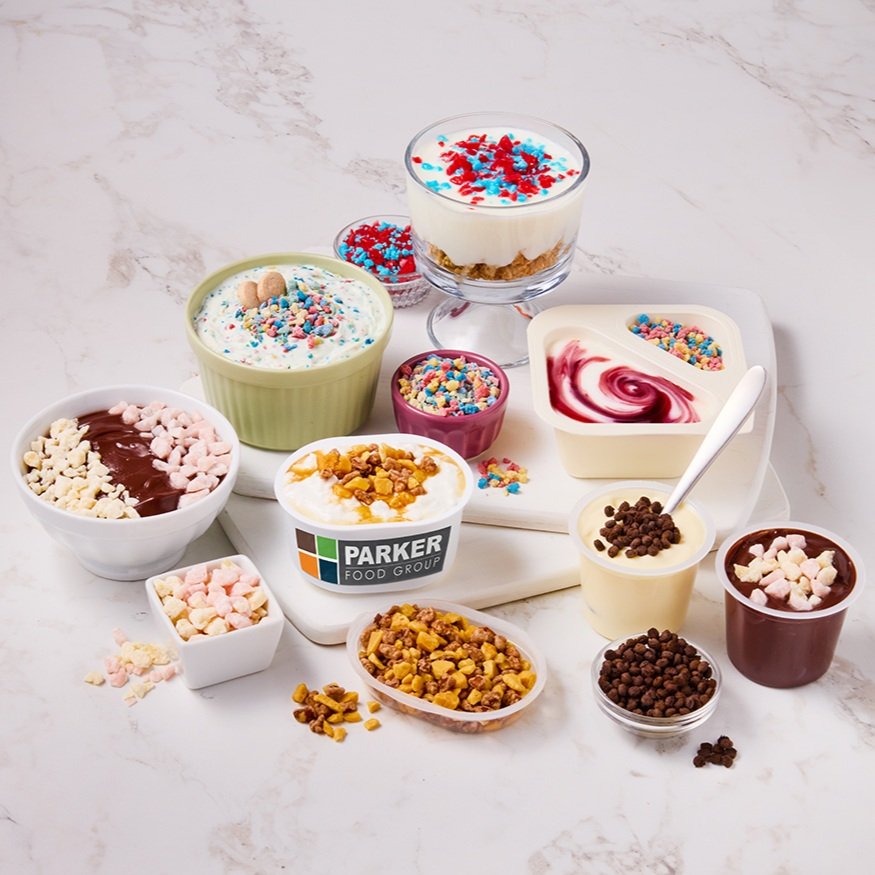 Assorted bowls and cups of yogurt with colorful sprinkles, cereal, and toppings on a white marble surface.