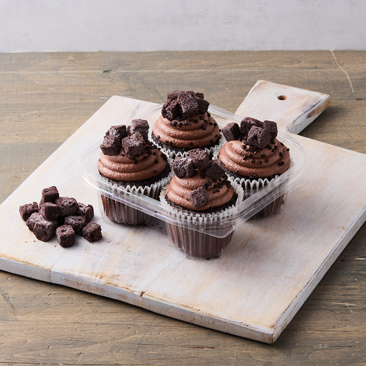 Four chocolate cupcakes topped with chocolate chunks on a white wooden cutting board with a serving of chocolate chunks beside them.