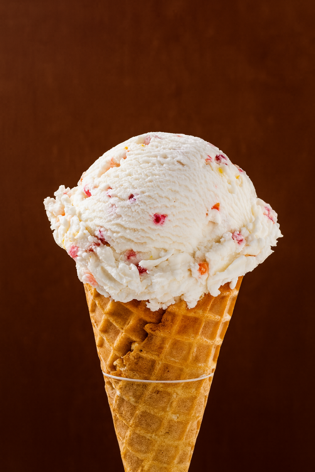Scoops of strawberry ice cream in a waffle cone against a plain dark brown background.