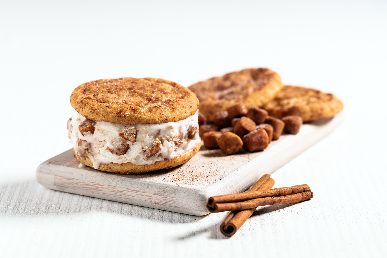Close-up of cookies with cream filling on a wooden board, with cinnamon sticks in the foreground, on a white background.