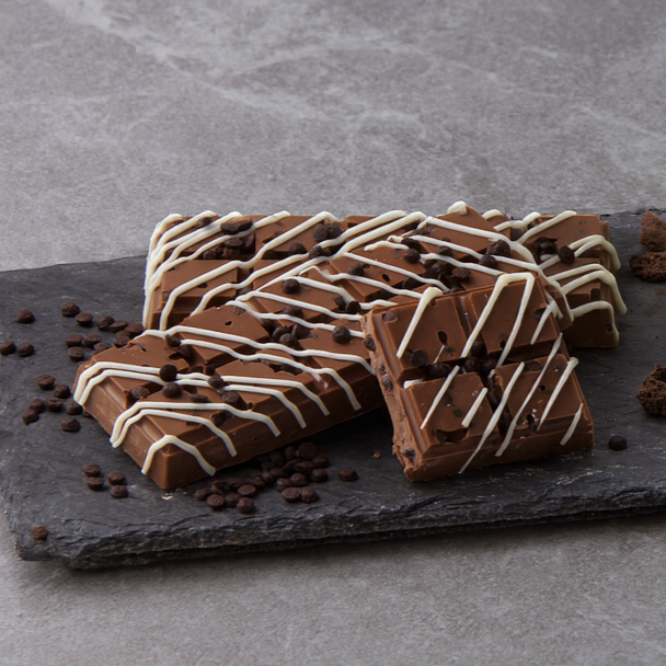 Several pieces of milk chocolate bark with white chocolate drizzle and chocolate chips on a dark slate serving board.