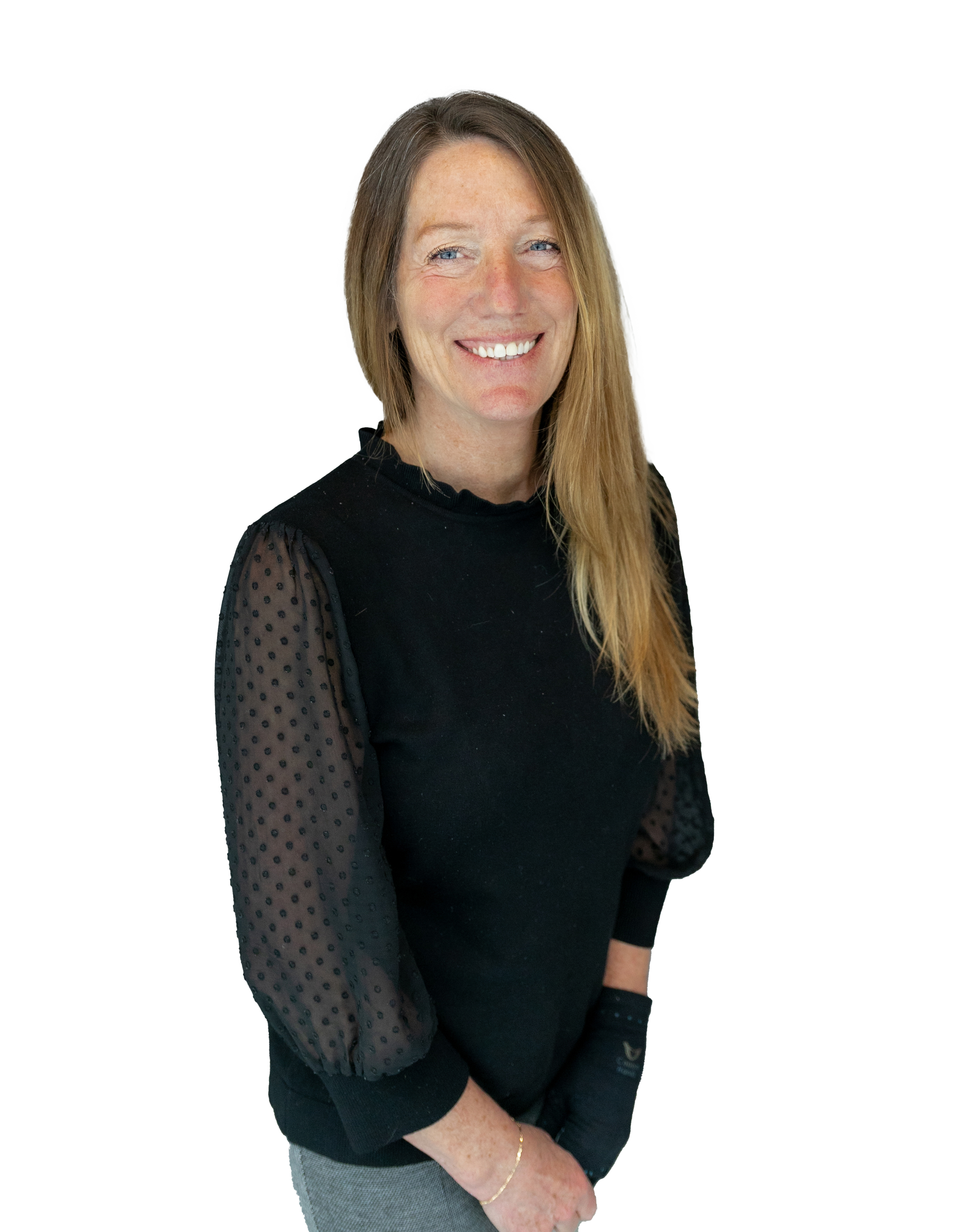A woman with long, light brown hair and blue eyes smiles while wearing a black top with sheer polka-dot sleeves and gray pants.