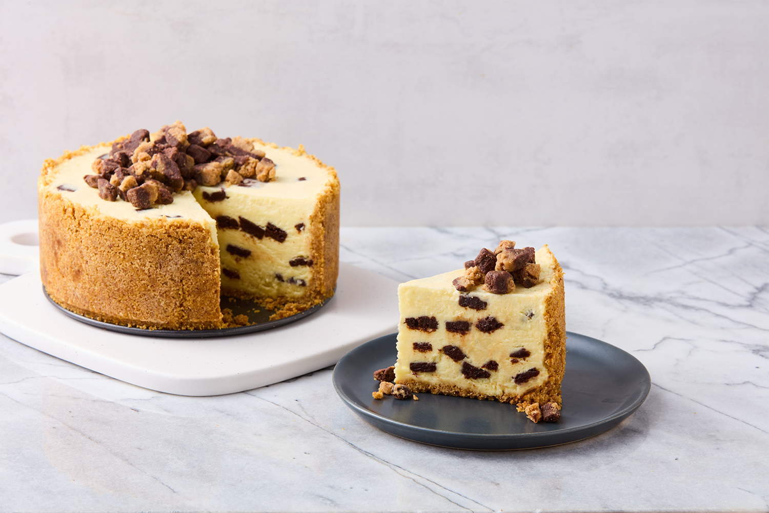Cheesecake with chocolate chunks and a crumbly exterior, with a slice on a black plate.