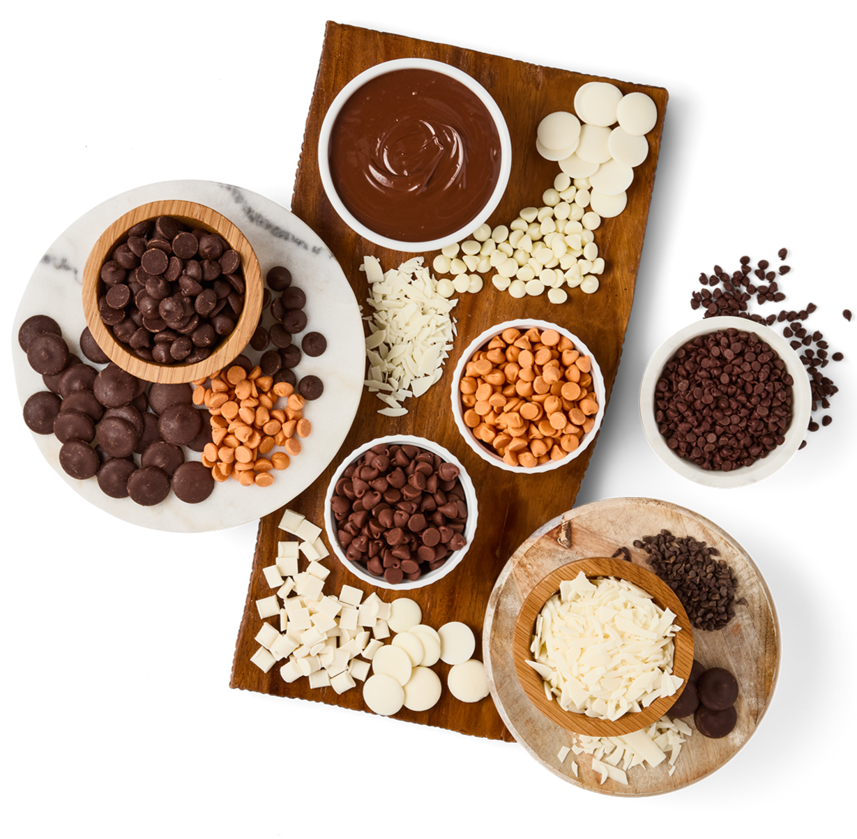Assorted chocolate chips, white and milk chocolate, in bowls and on plates, along with chocolate spread on a wooden board, displayed on a black surface.