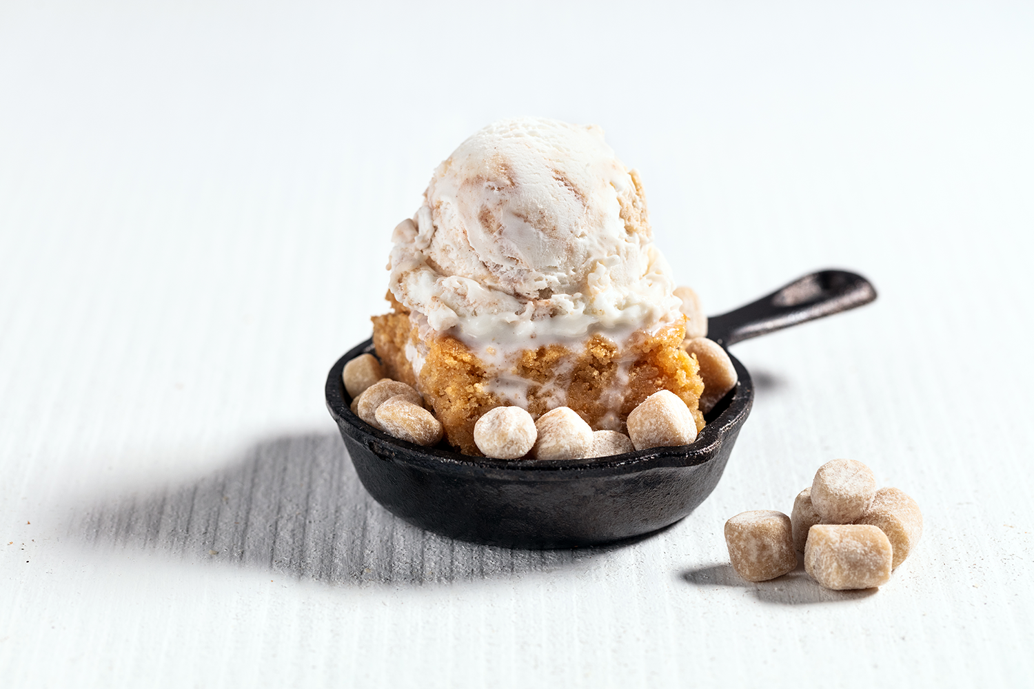 Scoops of vanilla ice cream on a crumbly dessert with marshmallows in a black skillet