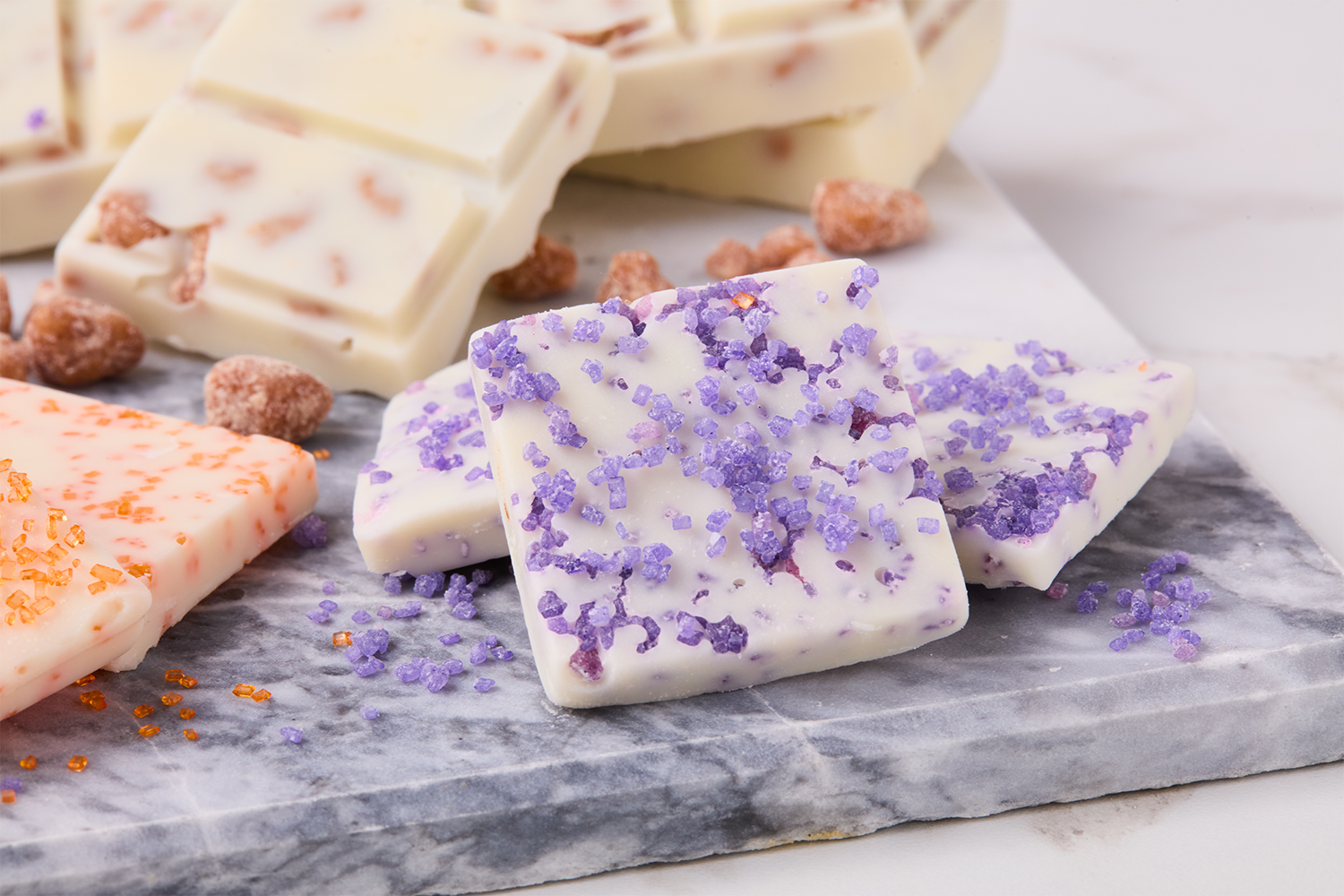 White chocolate bark with purple, orange, and pink sugar crystals on a marble surface.