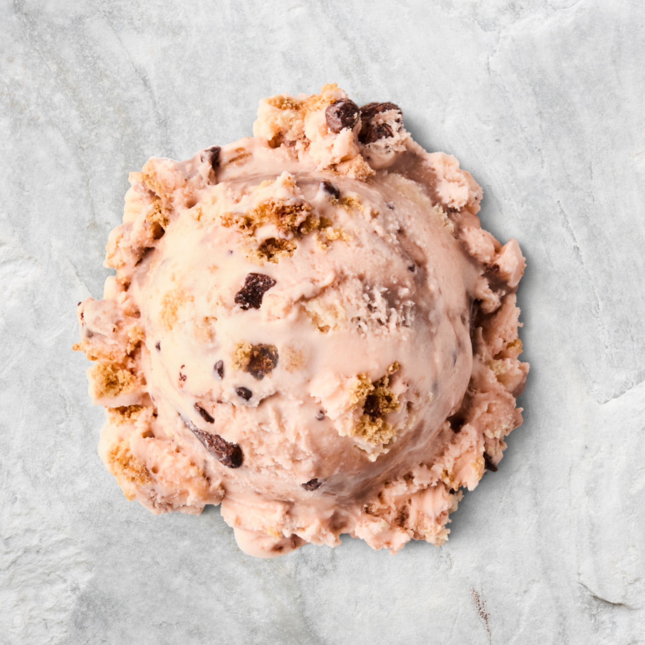 A scoop of cookies and cream ice cream with chocolate chunks on a textured surface