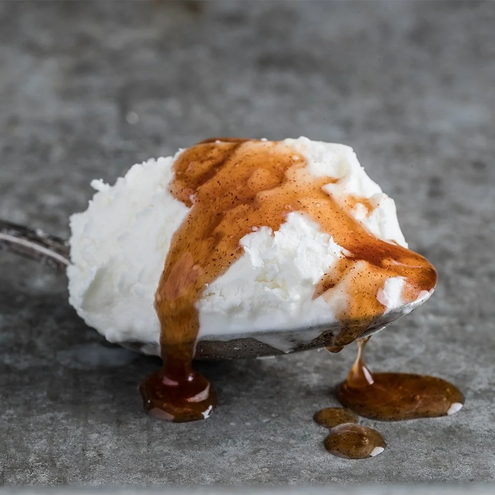 Scooped ice cream topped with caramel sauce on a gray surface.