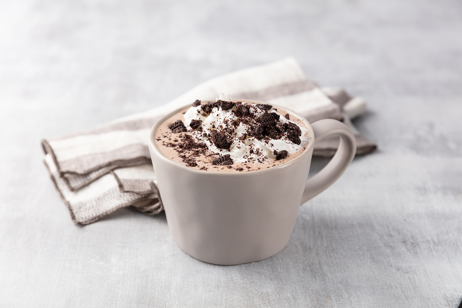 A white mug filled with hot chocolate topped with whipped cream and crushed cookies and creme.