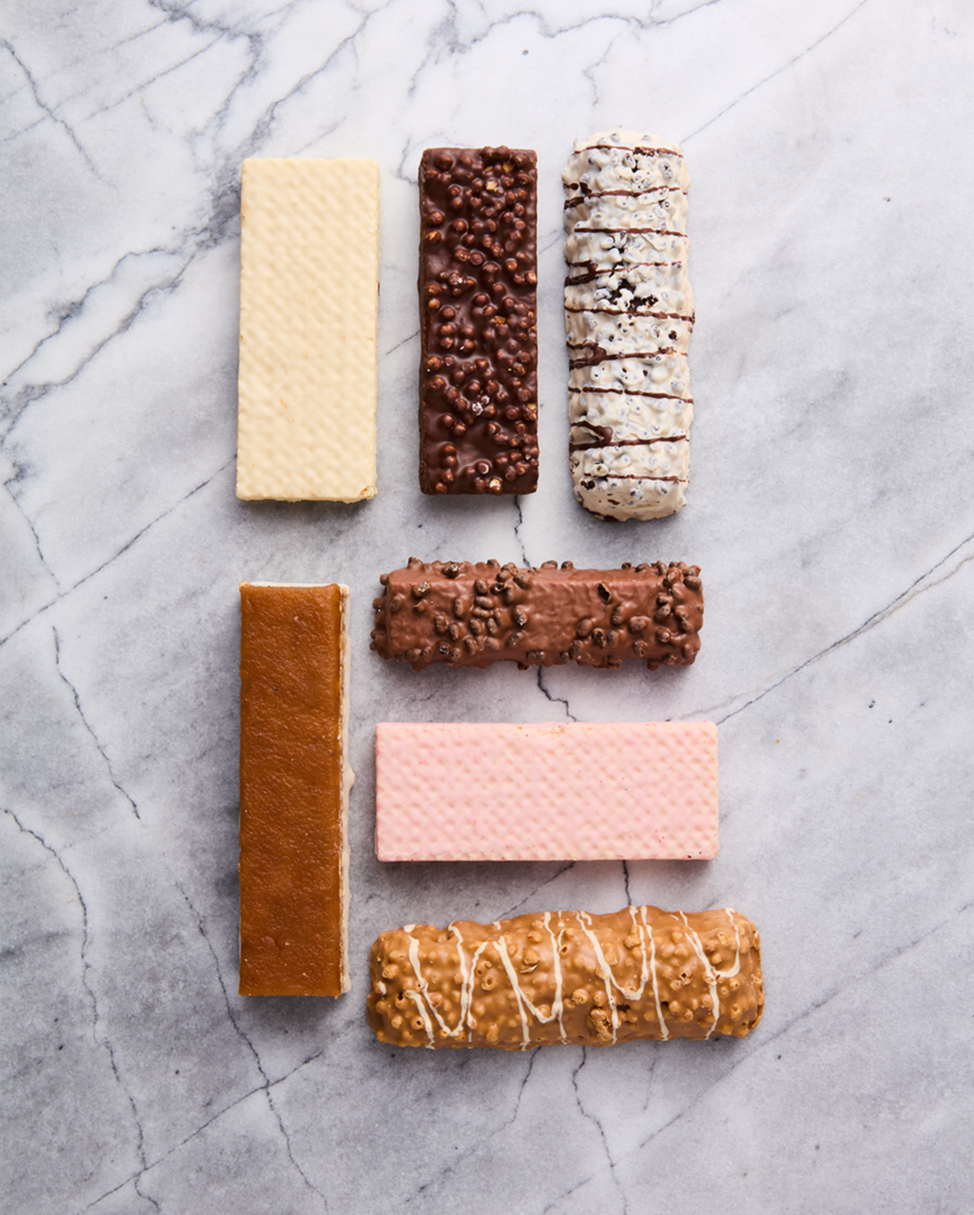 Seven assorted chocolate bars with various toppings and flavors arranged on a marble surface.